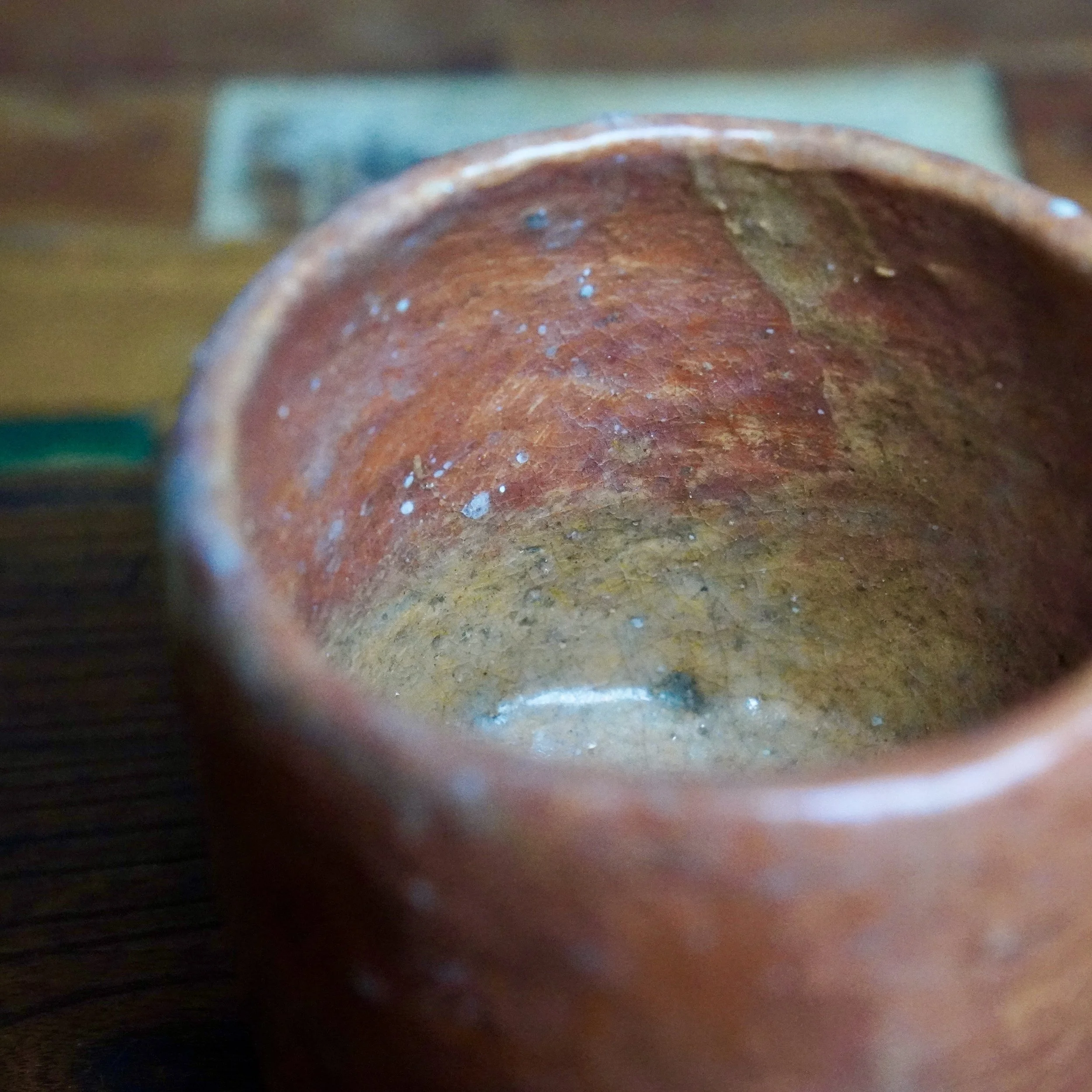 Interior of rustic reddish-brown ceramic bowl from Hioki Nanshū kiln, with white and blue speckles and a white drip mark on its yellow base.