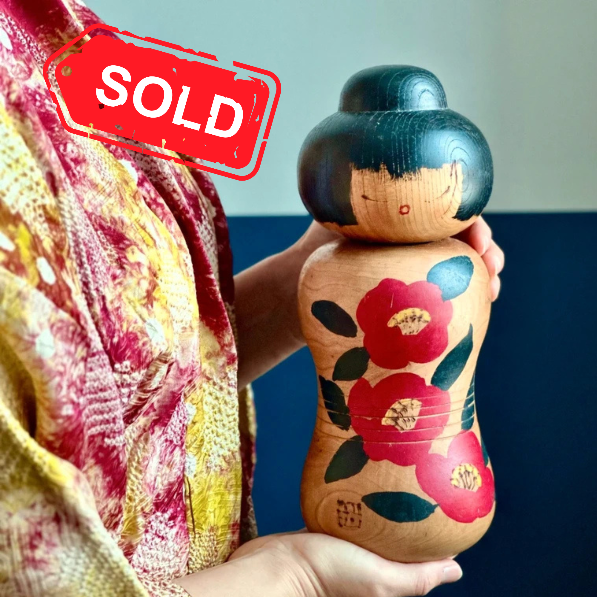 Large Sōsaku kokeshi by Tanaka Harumasa, tsubaki camellia, signed, Shōwa period, held in hands by woman wearing haori jacket