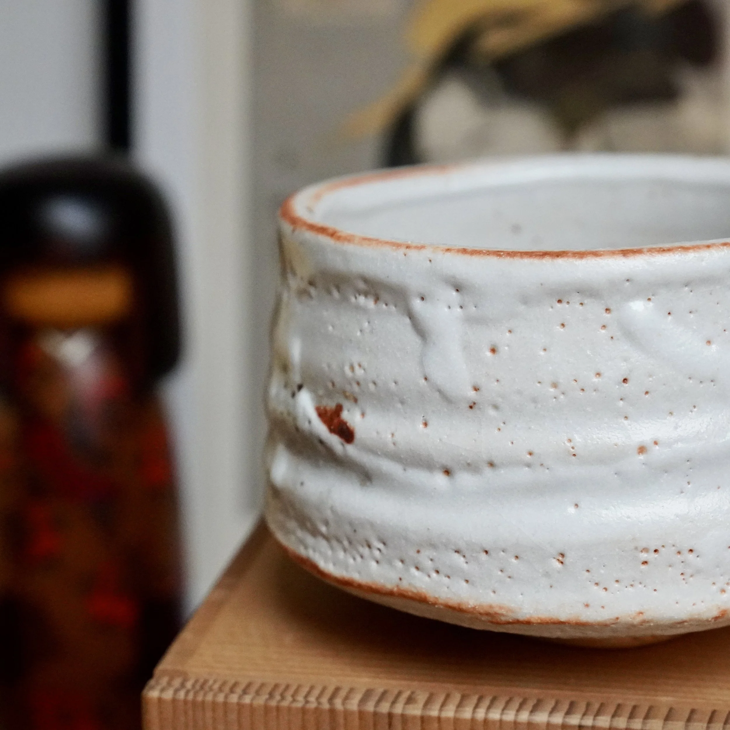 Shino chawan, close-up view of its rustic white, textured surface, and irregular rim with rust-orange glaze accents.