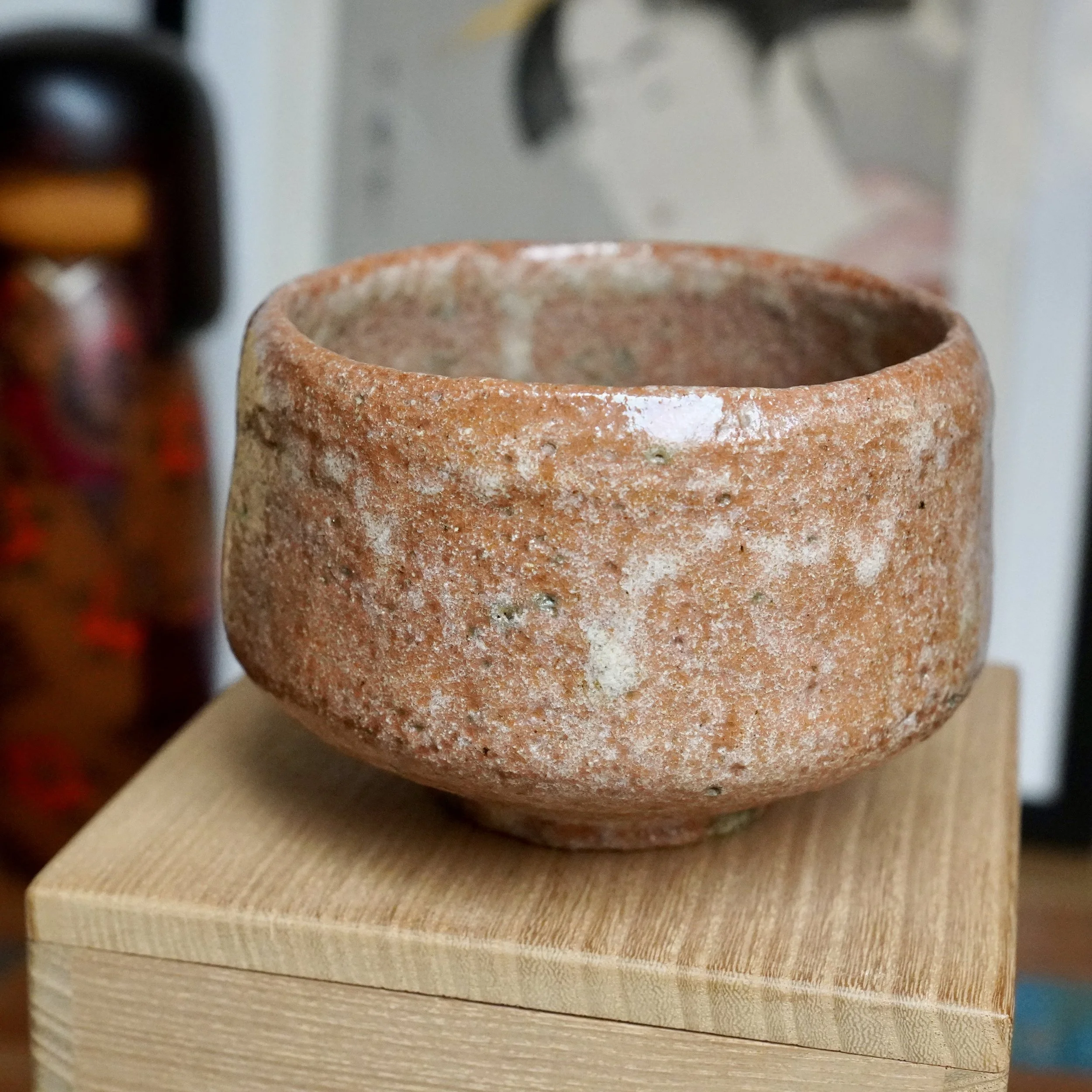 Sawada Hiroyuki's aka-raku chawan, a rugged reddish-orange bowl with sandy texture and prominent white glaze drips, on a wooden box.
