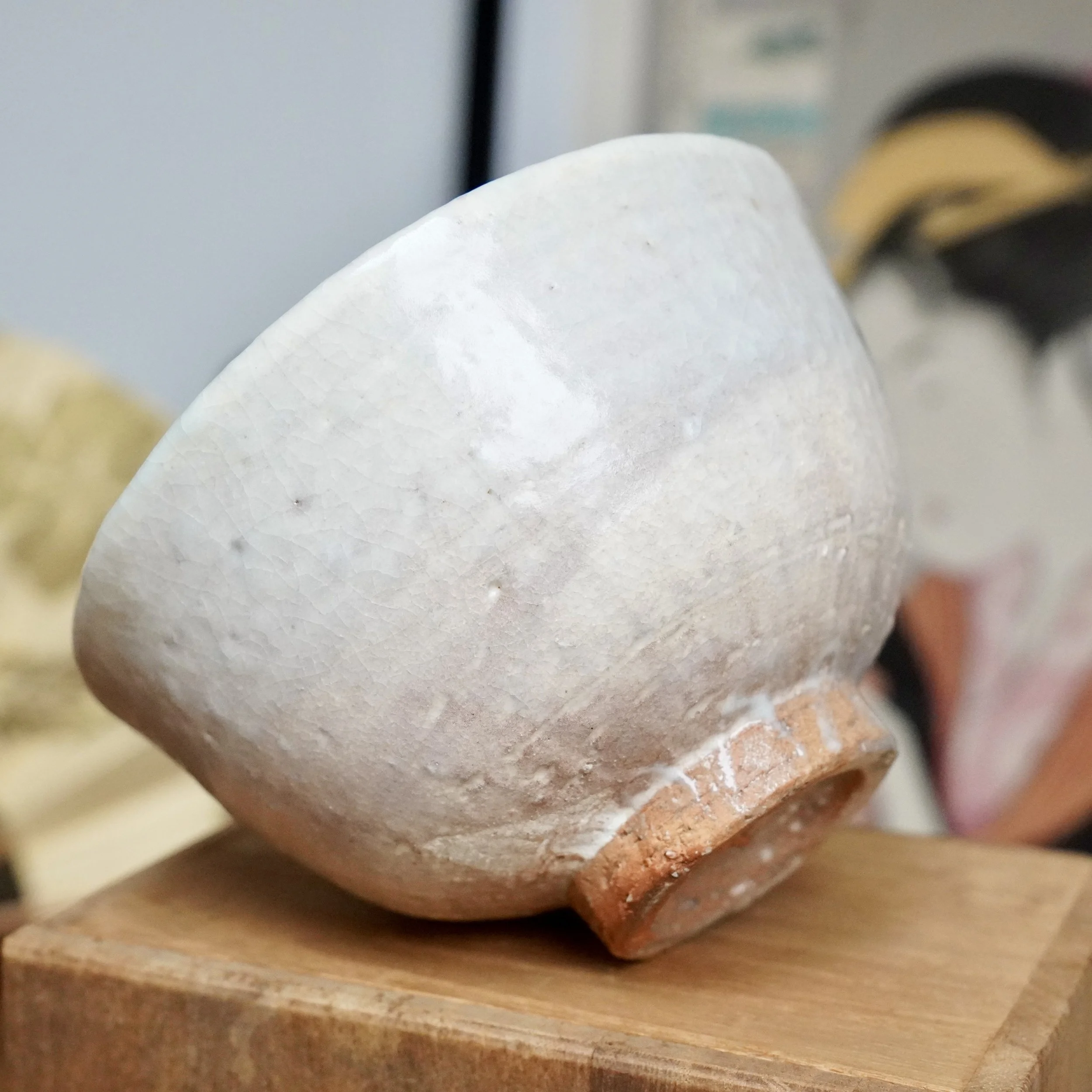 Hagi-yaki chawan by Tamamura Shōgetsu, tilted to show crackled white glaze with subtle stains, fading to a rough reddish-brown clay base on wood.