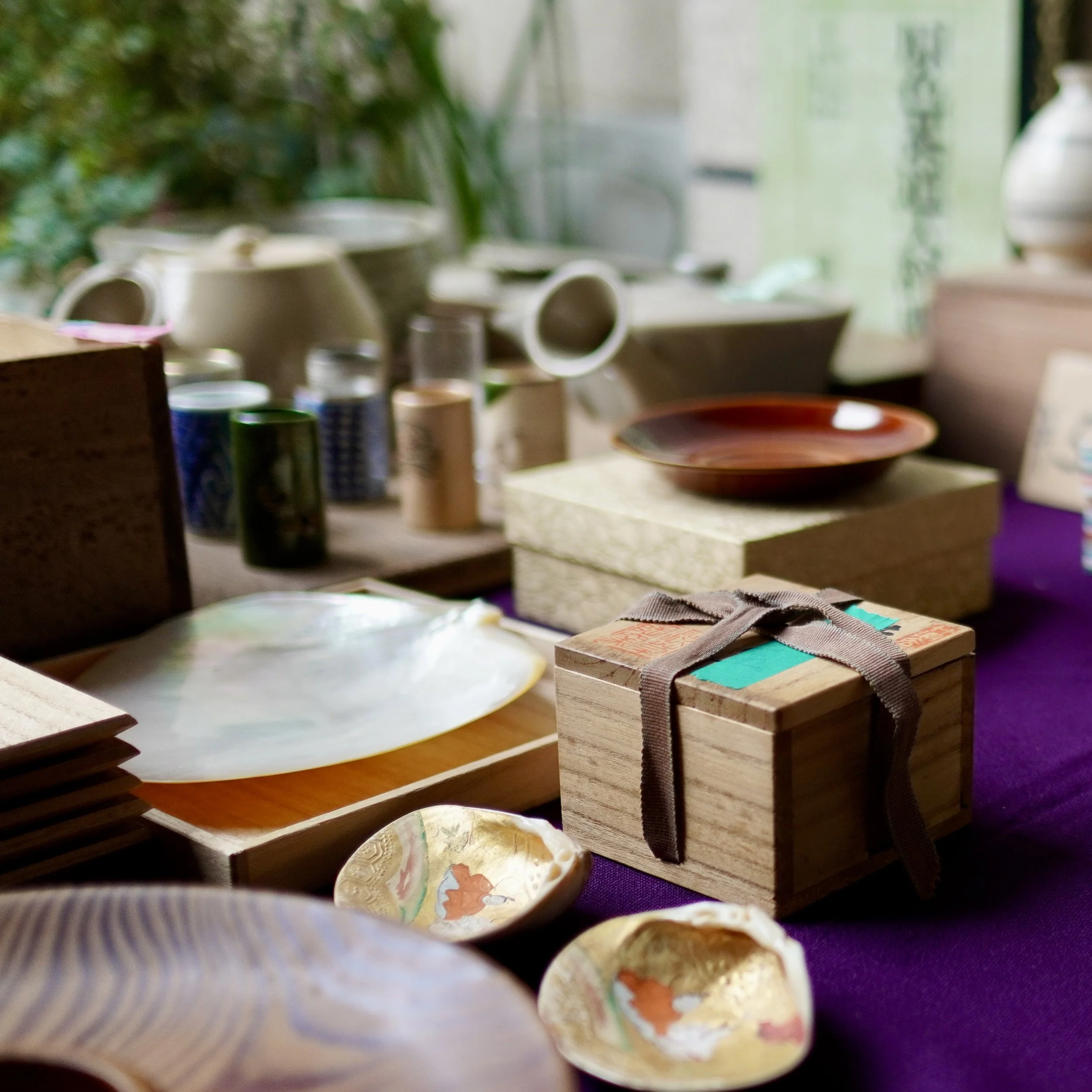 A close-up view of unique vintage Japanese items found at an antique market, including a tied wooden tomobako box with traditional ribbons, detailed gold-painted shell dishes, and polished lacquerware plates on a purple fabric background.