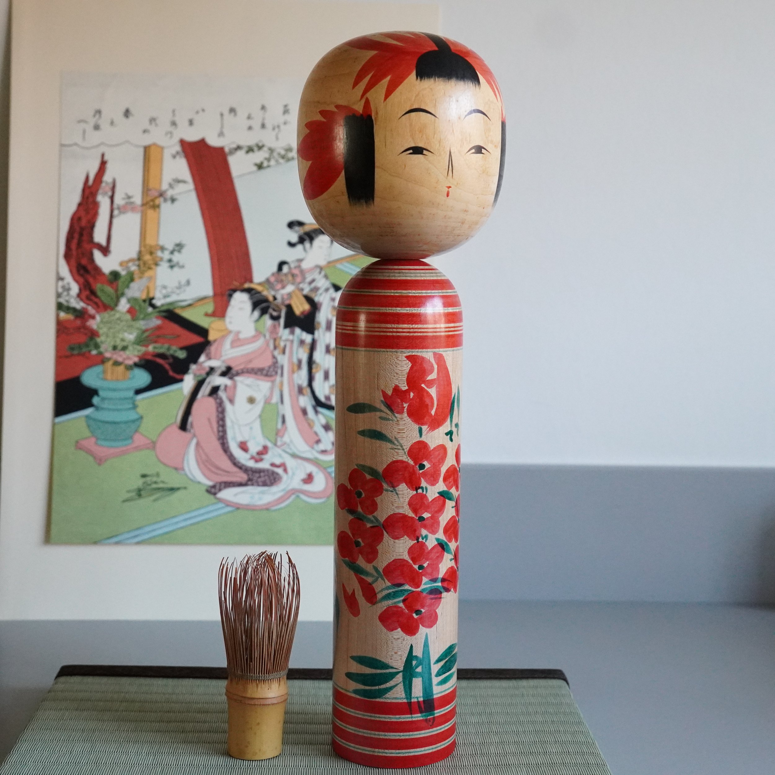 Yamagata-kei kokeshi by Takasaki Eiichirō shown at full height next to matcha whisk, red chrysanthemum motif visible, traditional Japanese wooden doll, Shōwa period