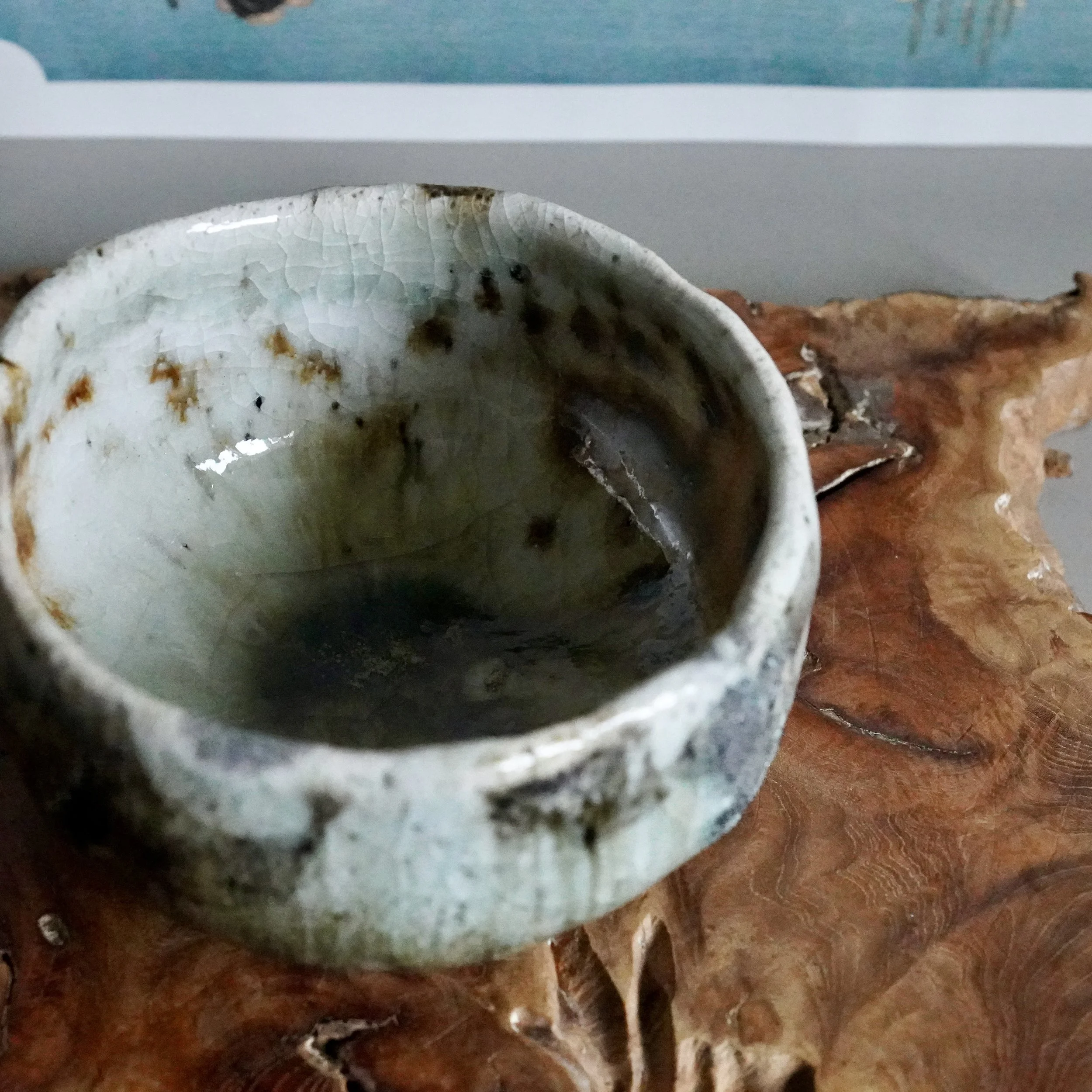 Deguchi Eiji wood-fired chawan, showing its crackled pale green and rust-brown exterior, with glimpses of a dark mossy green interior, resting on natural wood.
