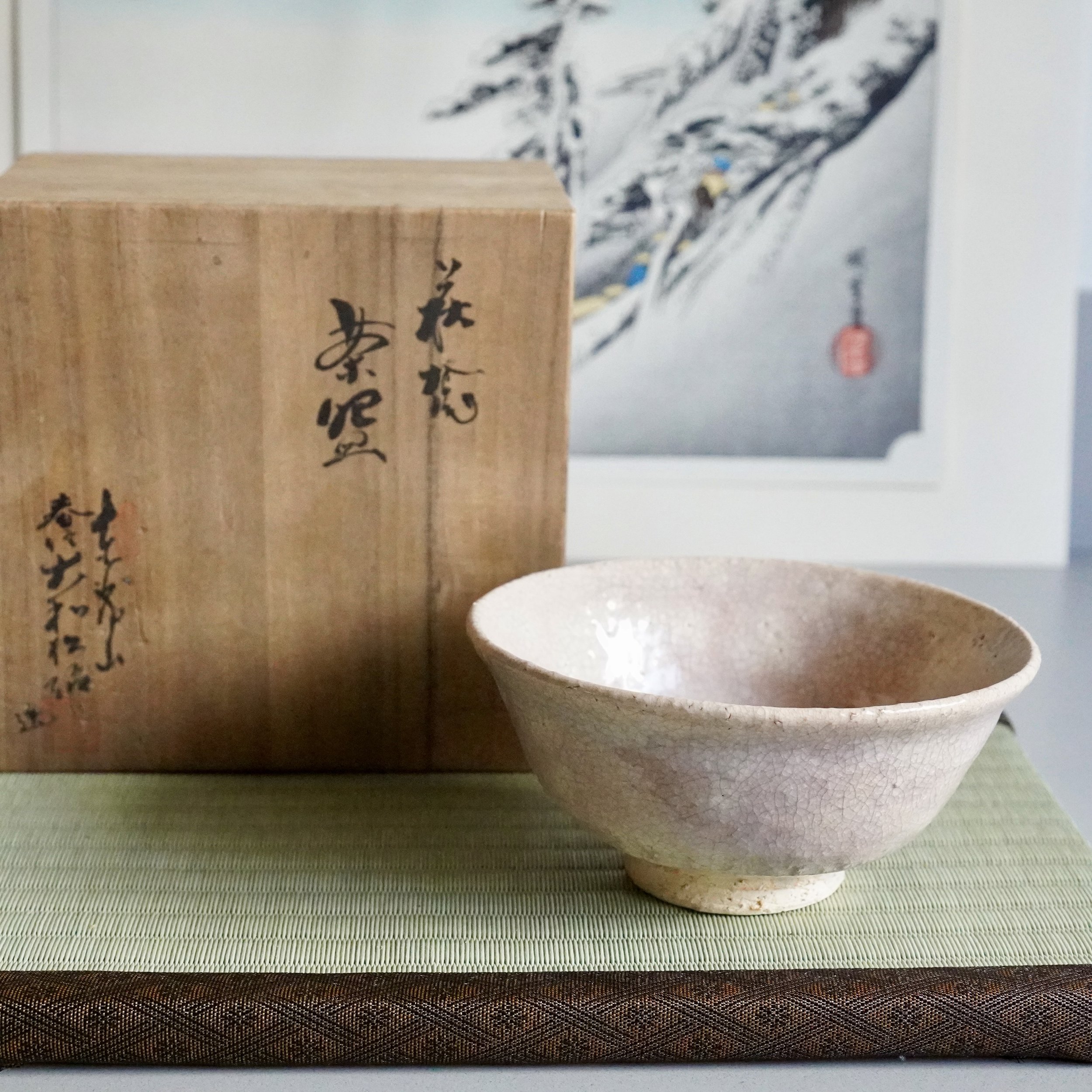 Hagi-yaki natsu-jawan matcha bowl beside signed tomobako wooden box, tatami mat, ukiyoe print background, Japan