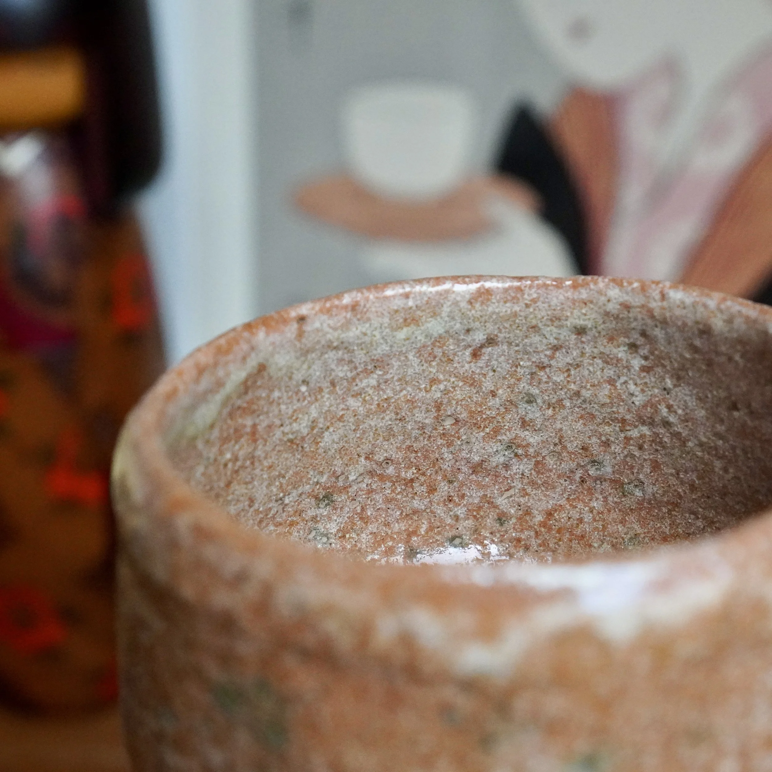 Close-up of aka-raku chawan interior by Sawada Hiroyuki, showing rugged reddish-orange surface with white glaze runs and green specks.
