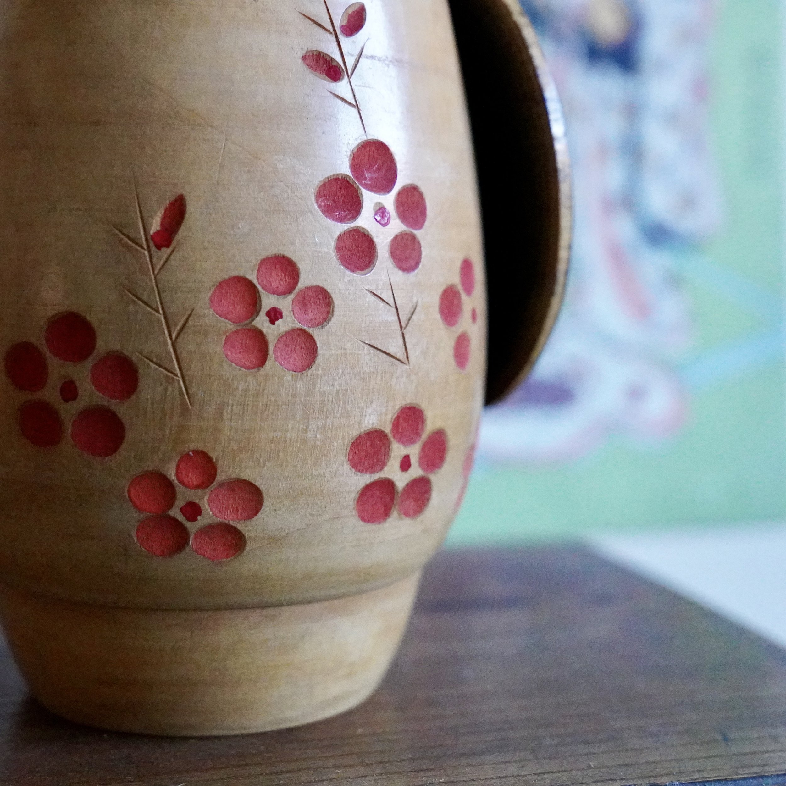Close up of carved red plum blossom clusters on Sato Suigai kokeshi, incised and pigment filled