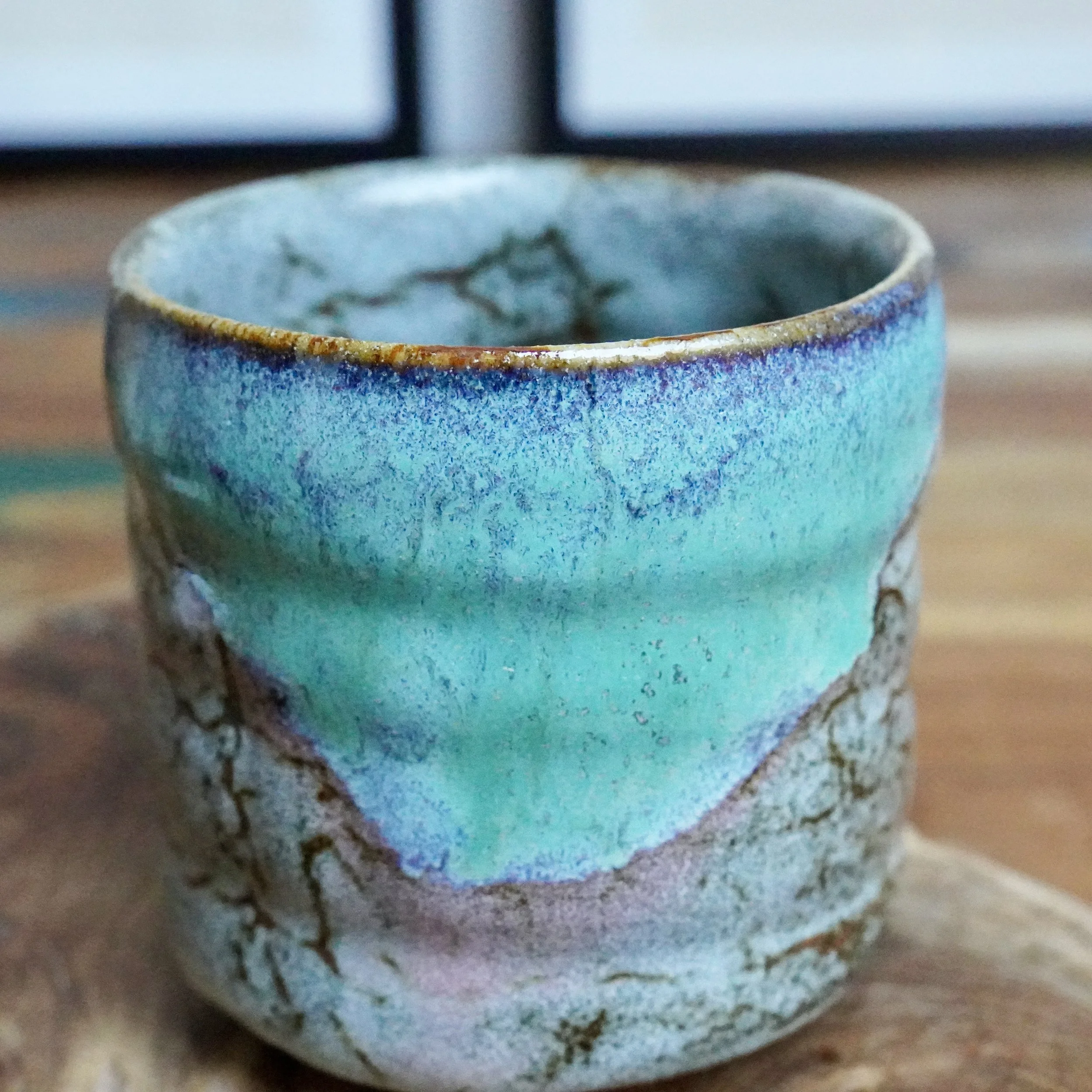Tsutsu chawan with a layered turquoise and grey glaze, featuring a warm brown rim and brown lines tracing its rustic textured lower body.