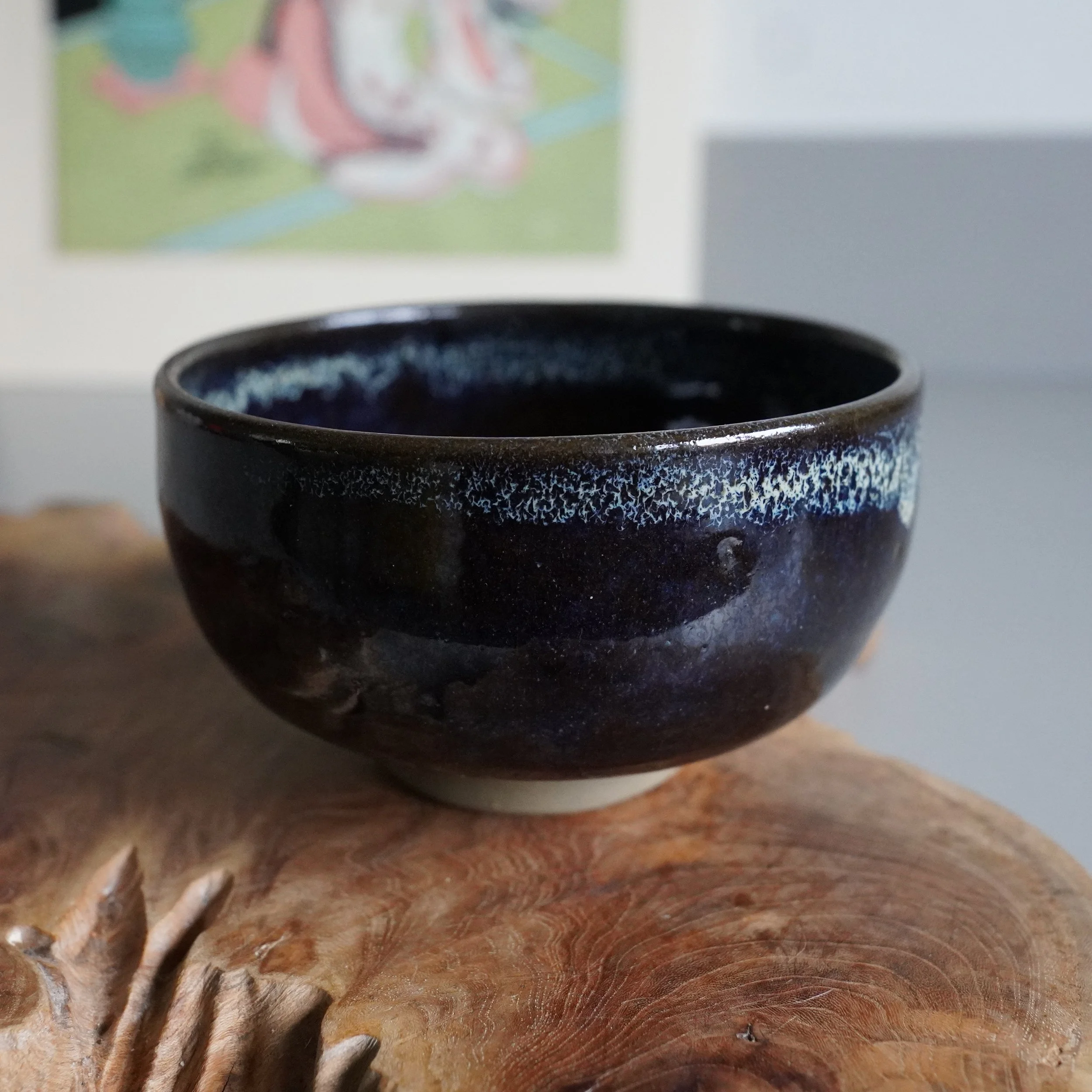 Rokuhō's Onta-yaki matcha bowl, deep brown with blue glaze patches and crackled texture near the rim, on a textured wooden surface.