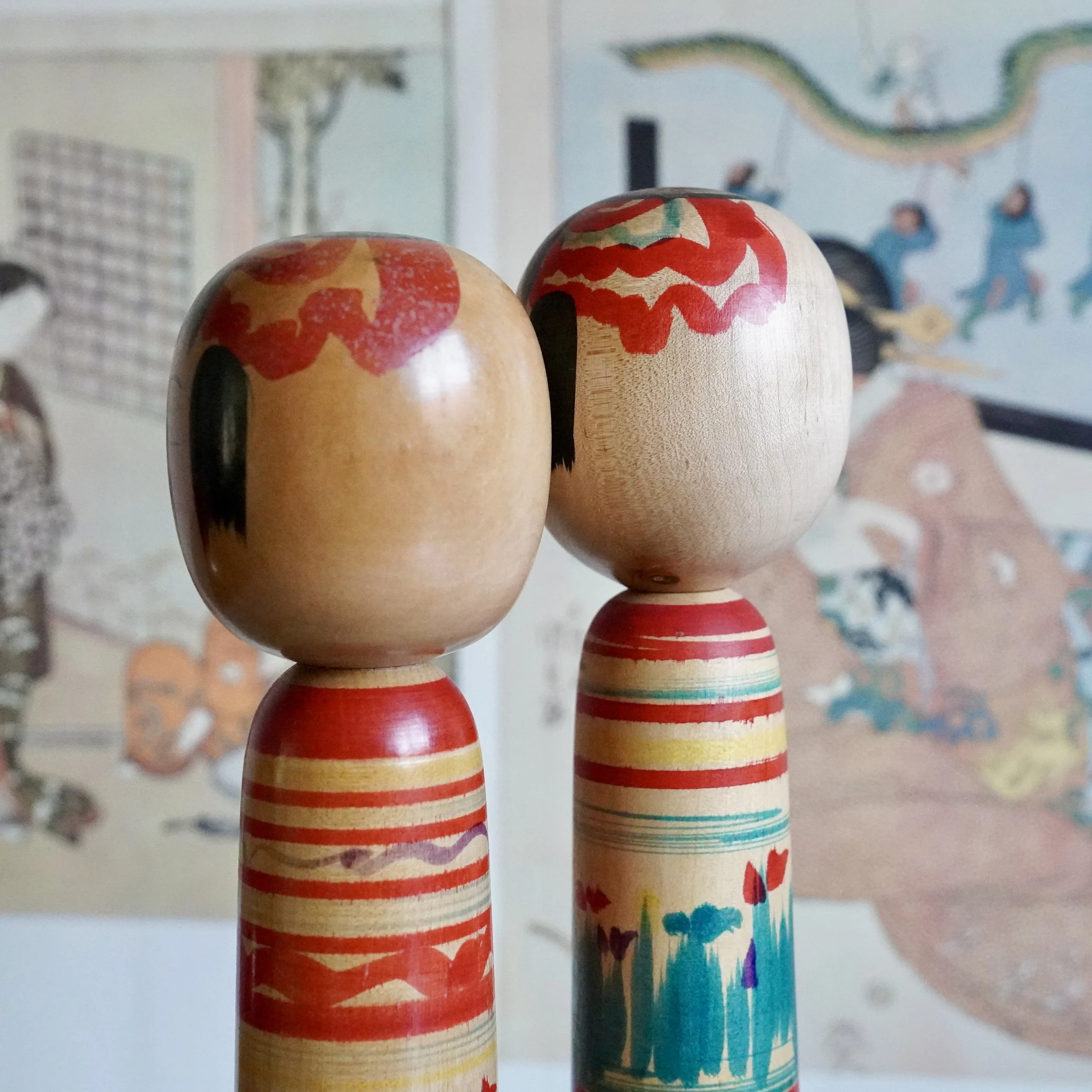 Back of head of Tsuchiyu kokeshi doll pair displayed against traditional Japanese woodblock print.