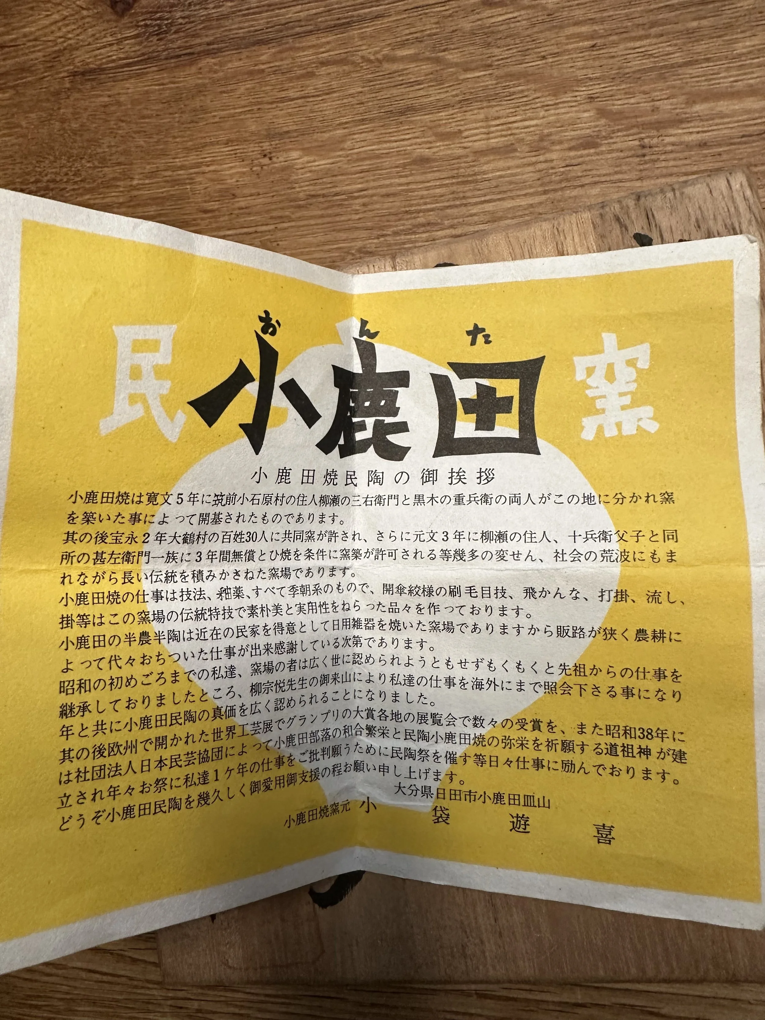 Folded yellow and white shiori for Rokuhō's Onta-yaki bowl, with black Japanese text, on a wooden surface.