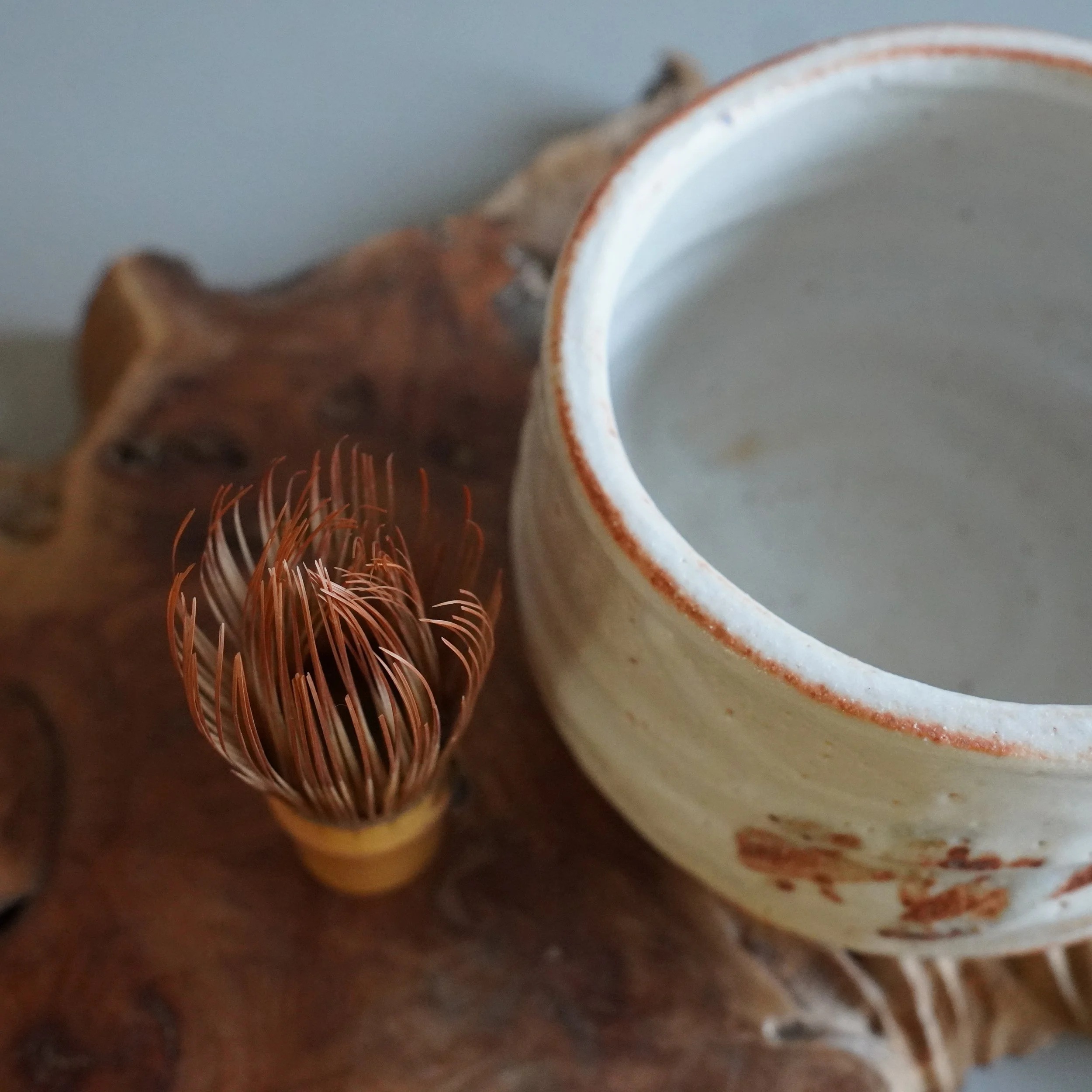 Deep Japanese winter chawan in Shino style, thick white glaze with iron-red clay visible at the rim, with a bamboo chasen whisk beside it. Vintage matcha bowl for the Japanese tea ceremony.