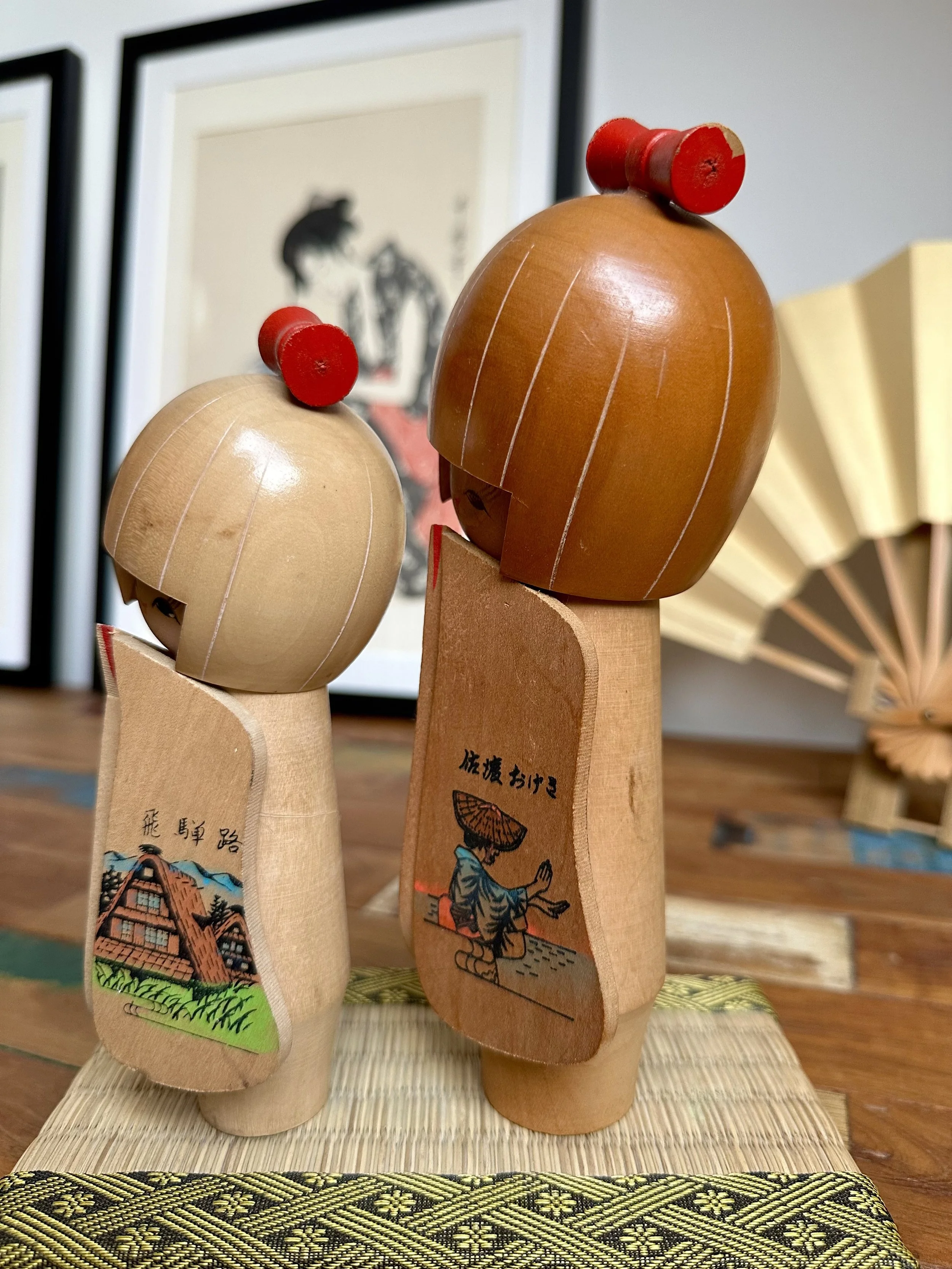 Side angle Hida Sado omiyage kokeshi pair panel inscriptions visible gold fan tatami mat Japan