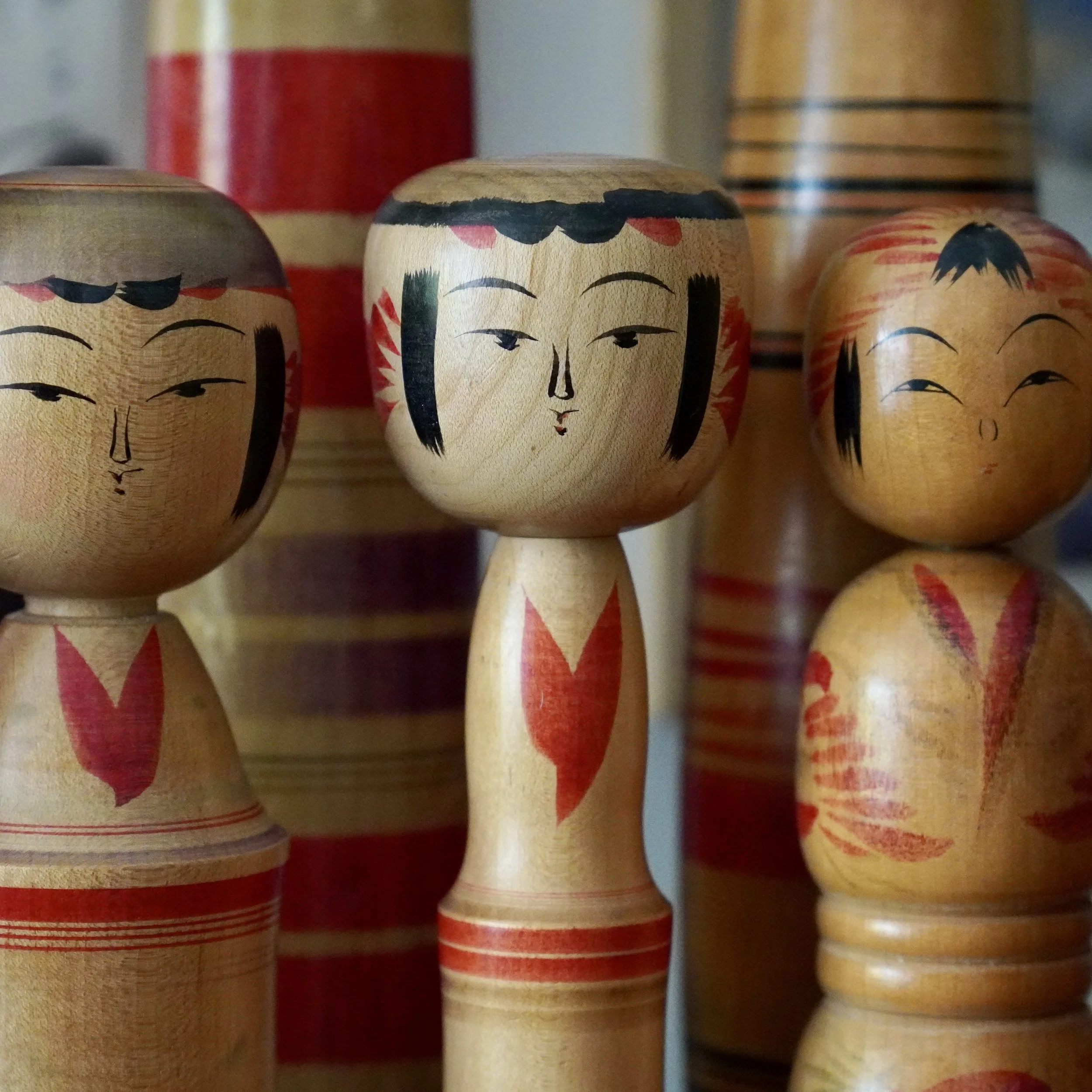 Yajirō and Tōgatta kokeshi faces compared, black hair sweeps versus red tegara sunburst crown, Inoue Harumi and Agatsuma Satoshi