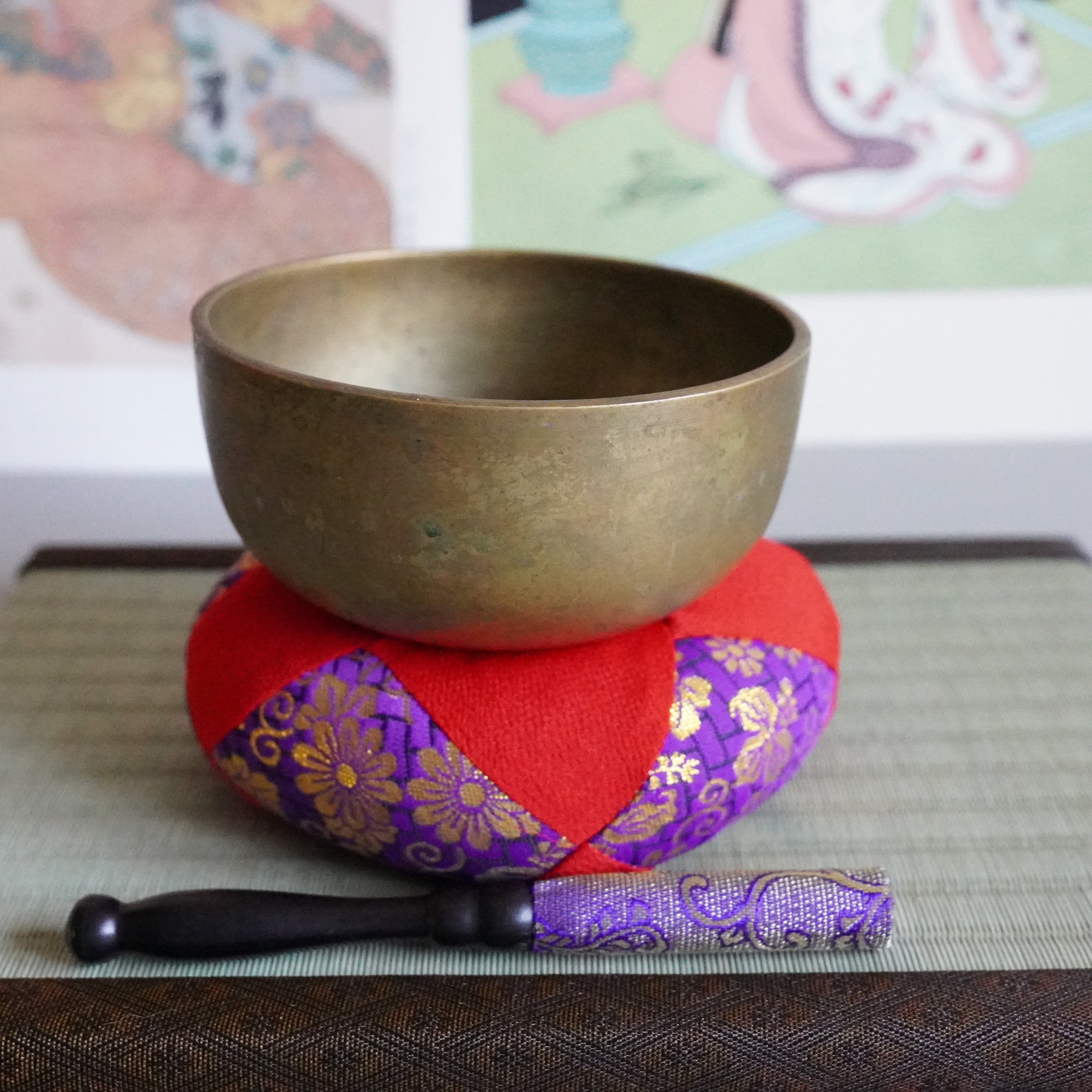 Bronze orin singing bowl on red and purple brocade cushion with striker, tatami mat