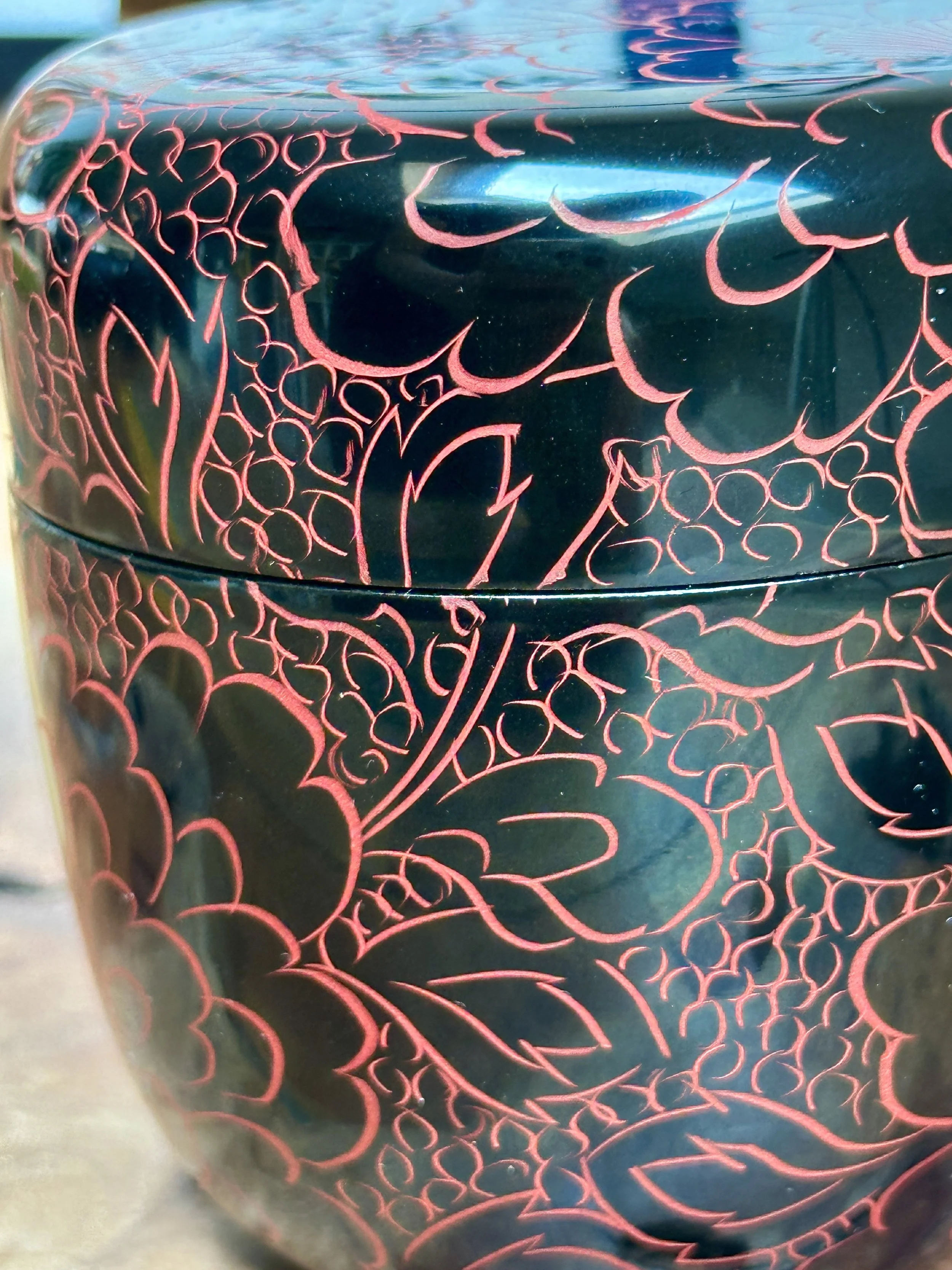 Lacquered tea caddy by Fujiwara Seiu, close-up of dark, glossy surface with intricate red engraved floral patterns on body and lid.
