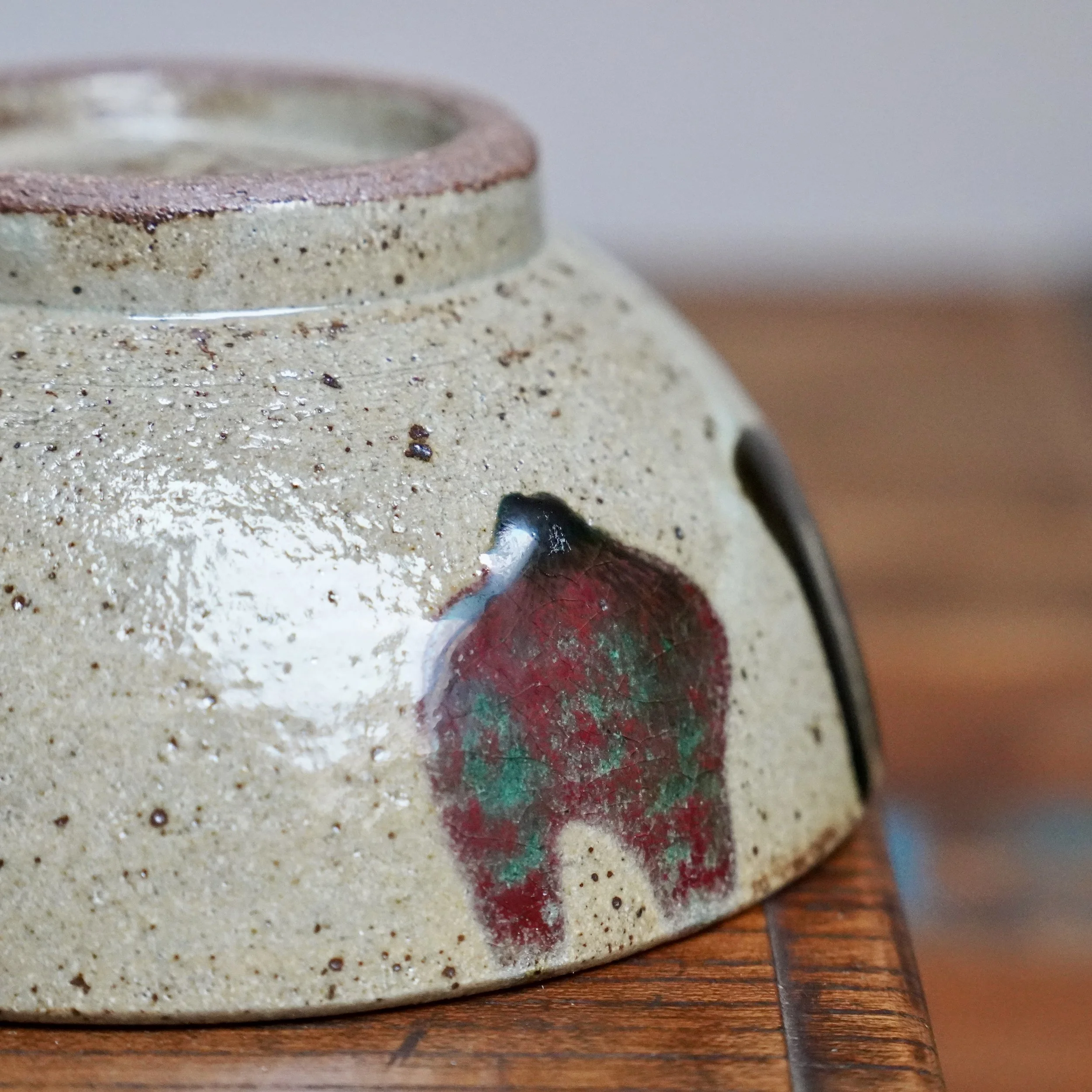 Inverted Kuromuta-yaki tea bowl, side view. Speckled grey clay, white glaze drips, thick black glaze, and a glowing wine-red & green decoration by Maruta Nobumasa kiln.