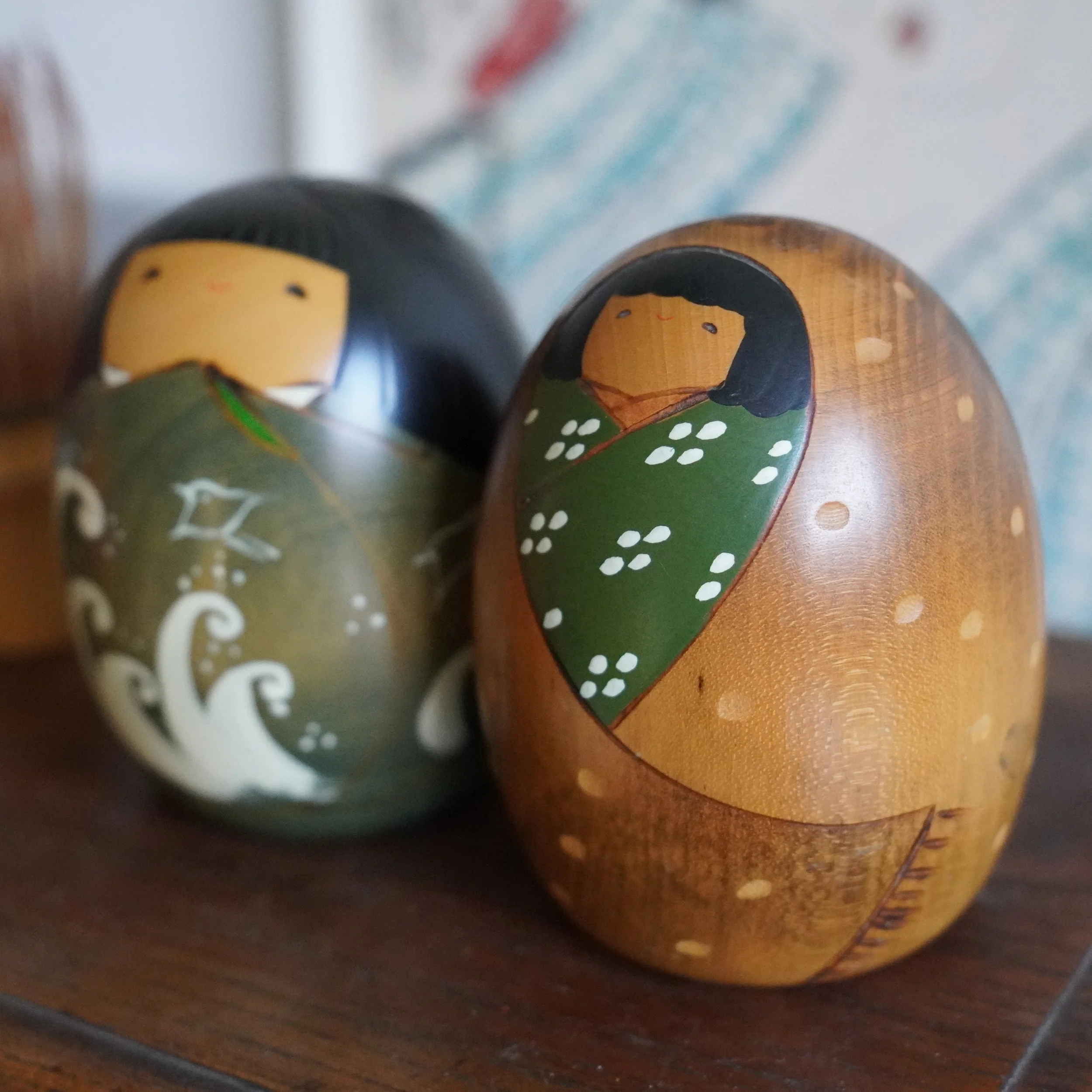 Close up front view of vintage Usaburo kokeshi pair, hand painted faces, summer and winter motifs, Showa period