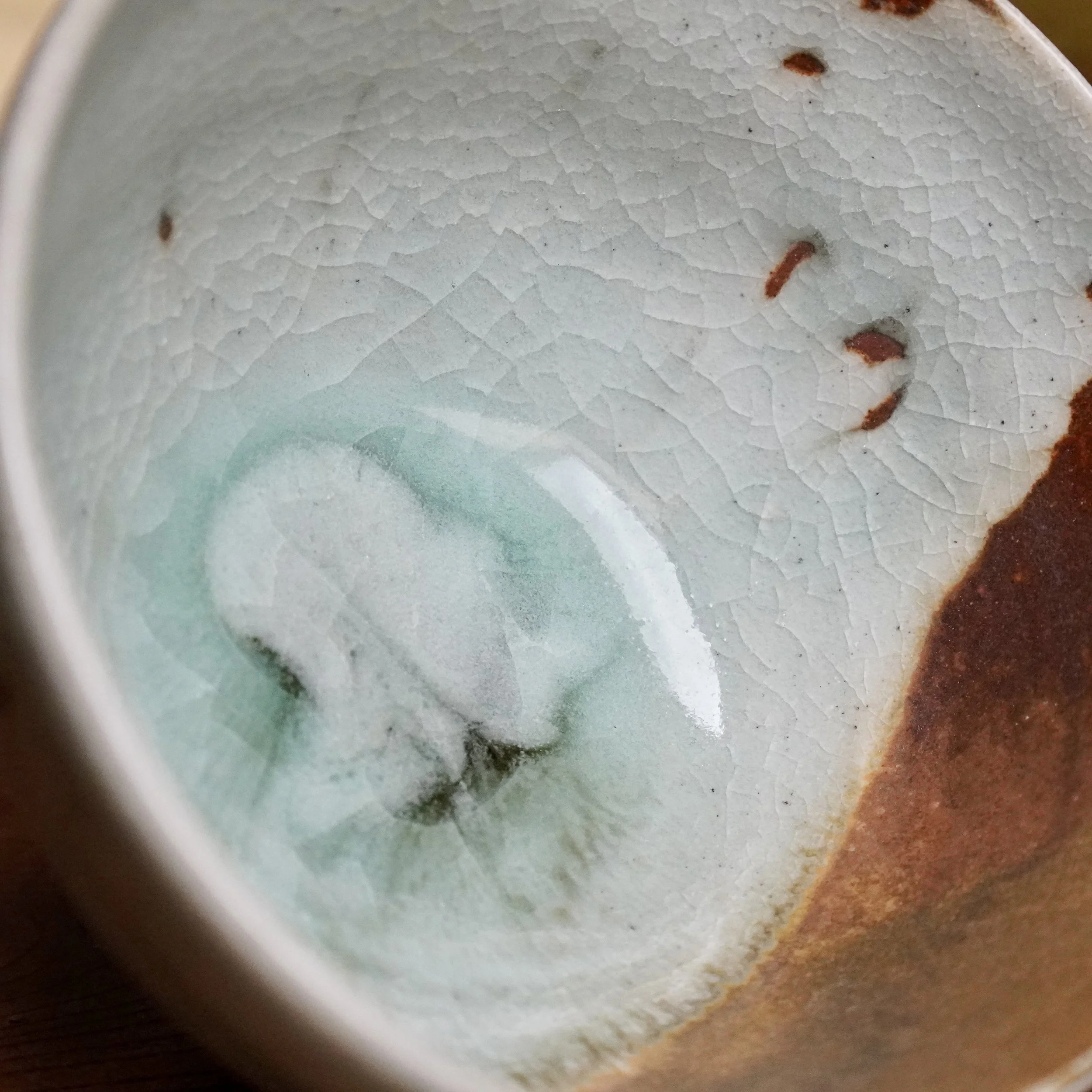 Close-up of a chawan interior, featuring pale blue ice crackle glaze merging into a warm rust-brown iron oxide glaze with subtle ochre streaks.