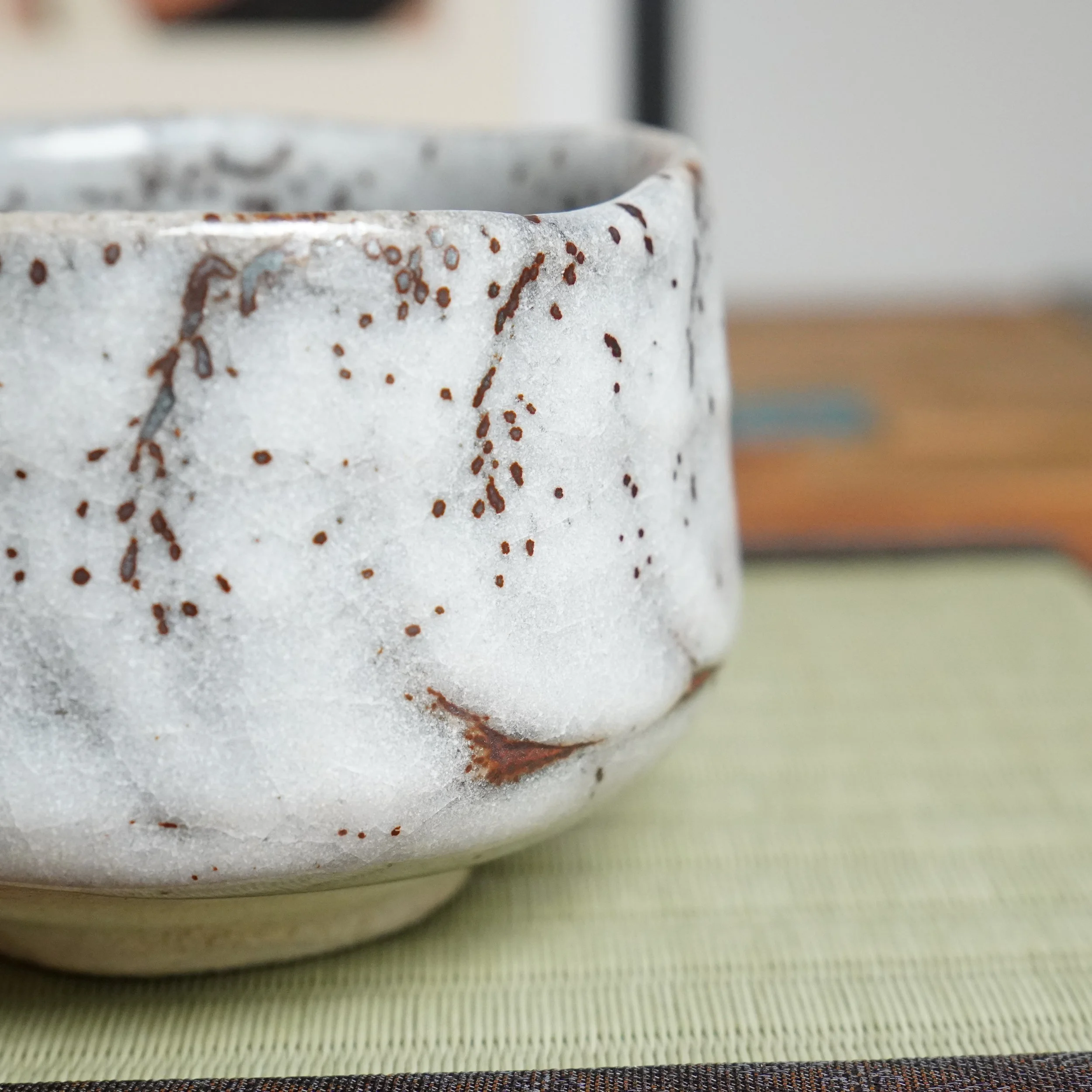 Oni-Shino chawan by Katō Shōzan, showing white glaze with rust-brown speckles and drips on its textured, hand-formed side.