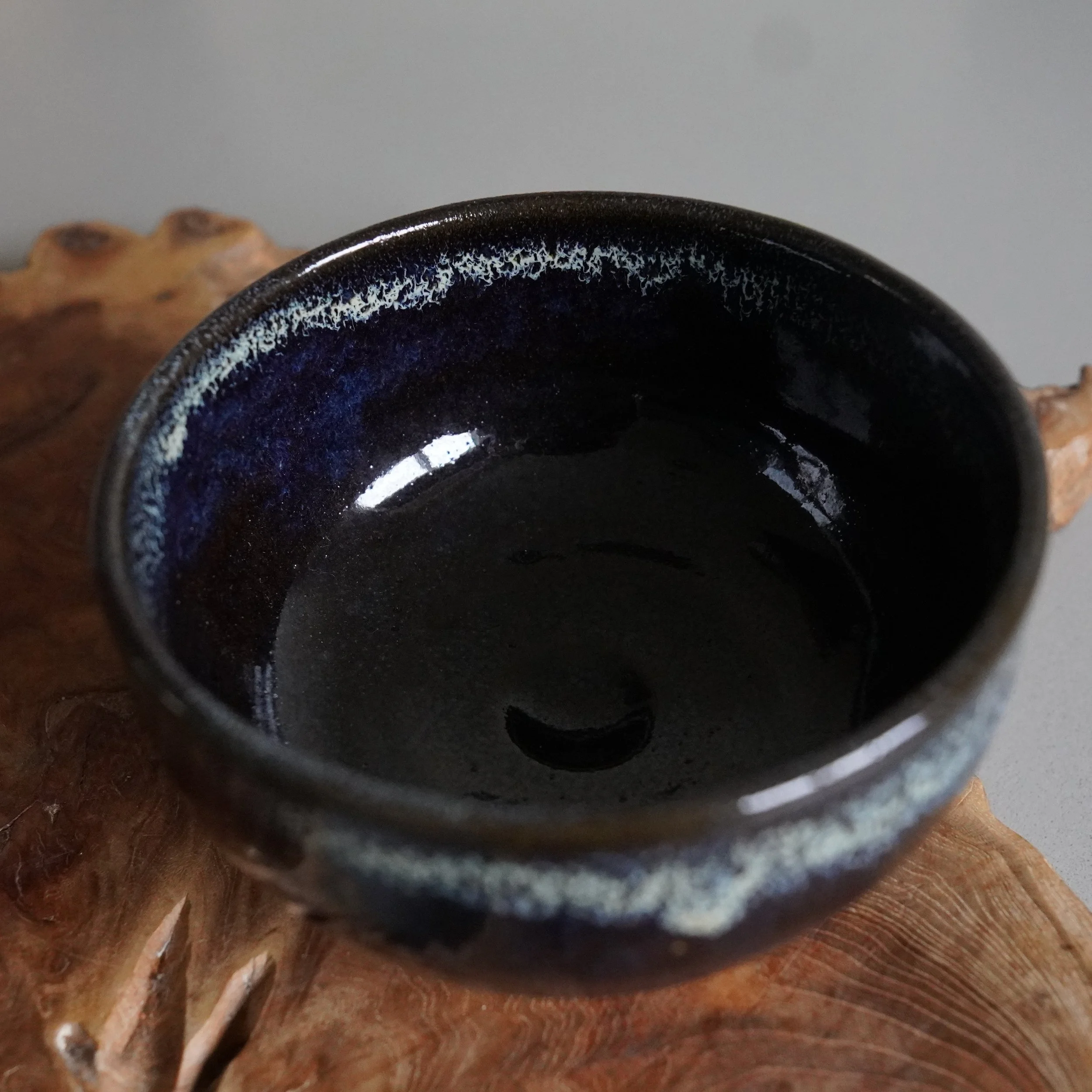 Rokuhō's Onta-yaki matcha chawan with deep blue-brown glaze and mottled white and blue patterns around its rim, resting on wood.