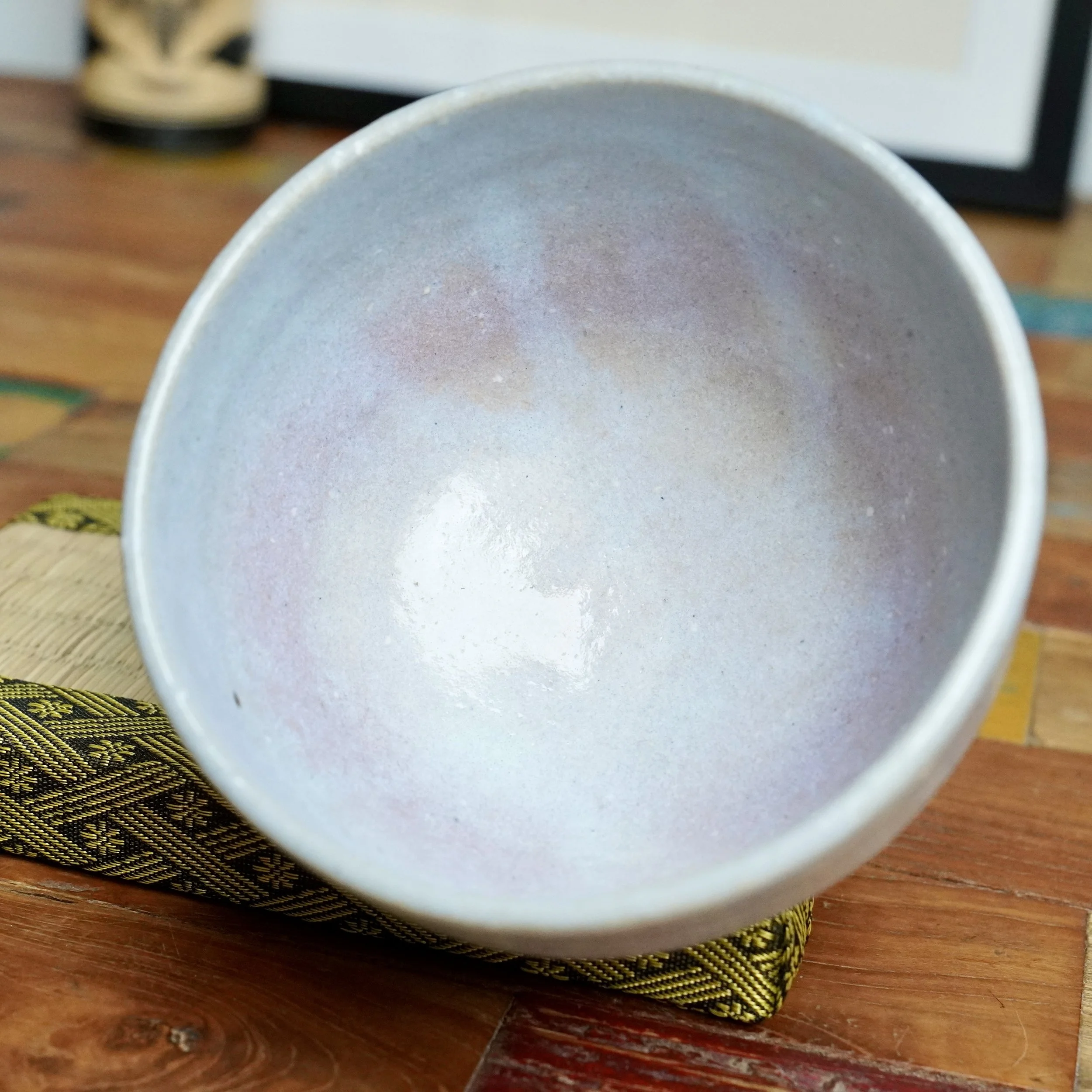 Moriwaki Fumitada's Hagi-yaki chawan, interior showing soft white glaze shifting to blue-grey and pale lilac, on a dark green and gold patterned mat.