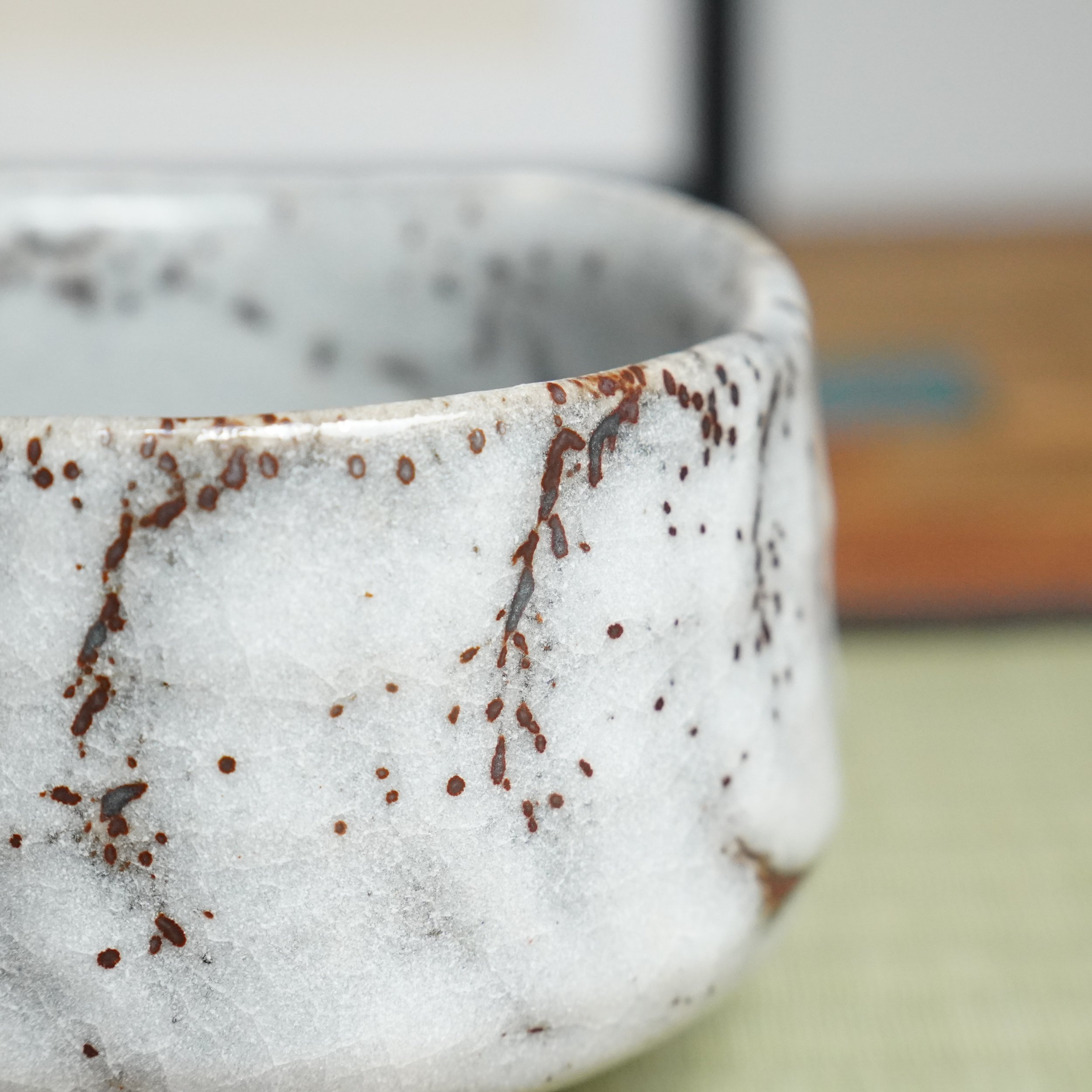 Oni-Shino chawan by Katō Shōzan, side view of thick white glaze with dense rust brown speckles and vertical drips.