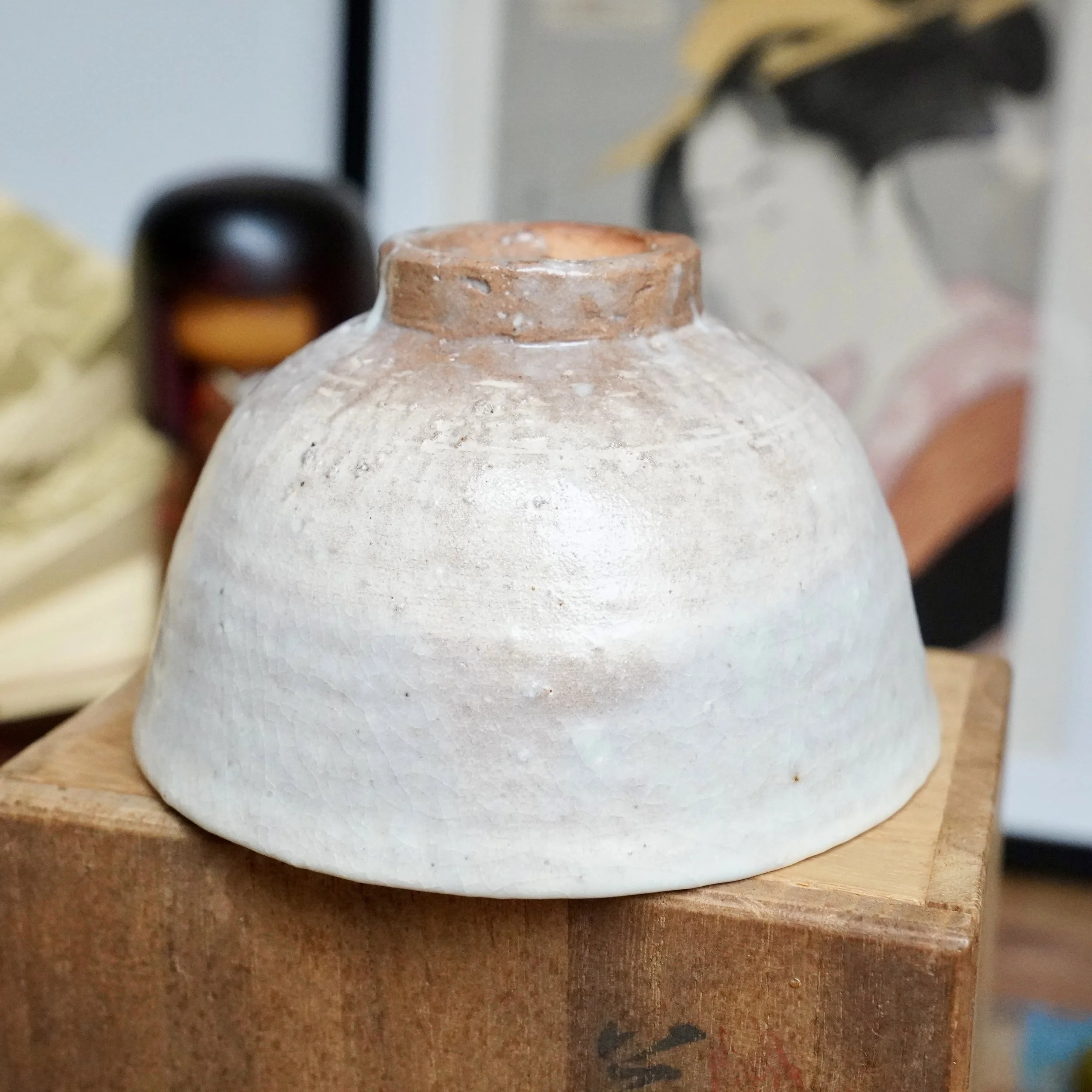 Hagi-yaki chawan by Tamamura Shōgetsu, placed upside down on a wooden box, showing its crackled off-white glaze and unglazed reddish-brown foot and rim.