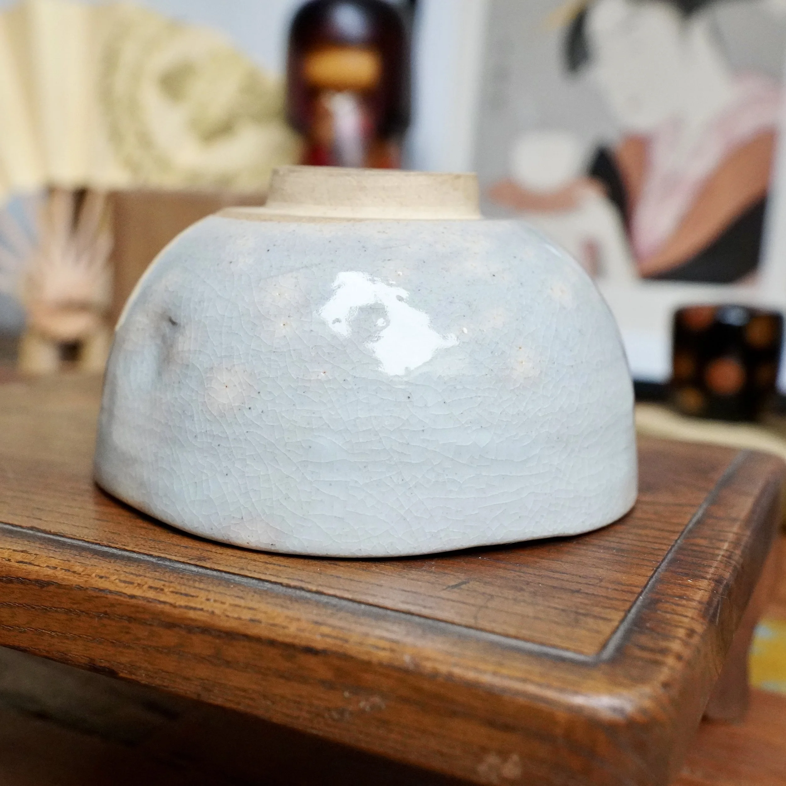 Nagasawa Minoru's Izushi-gama chawan, soft grey-blue crackled glaze with subtle pink blush, resting on a warm-toned wooden surface.