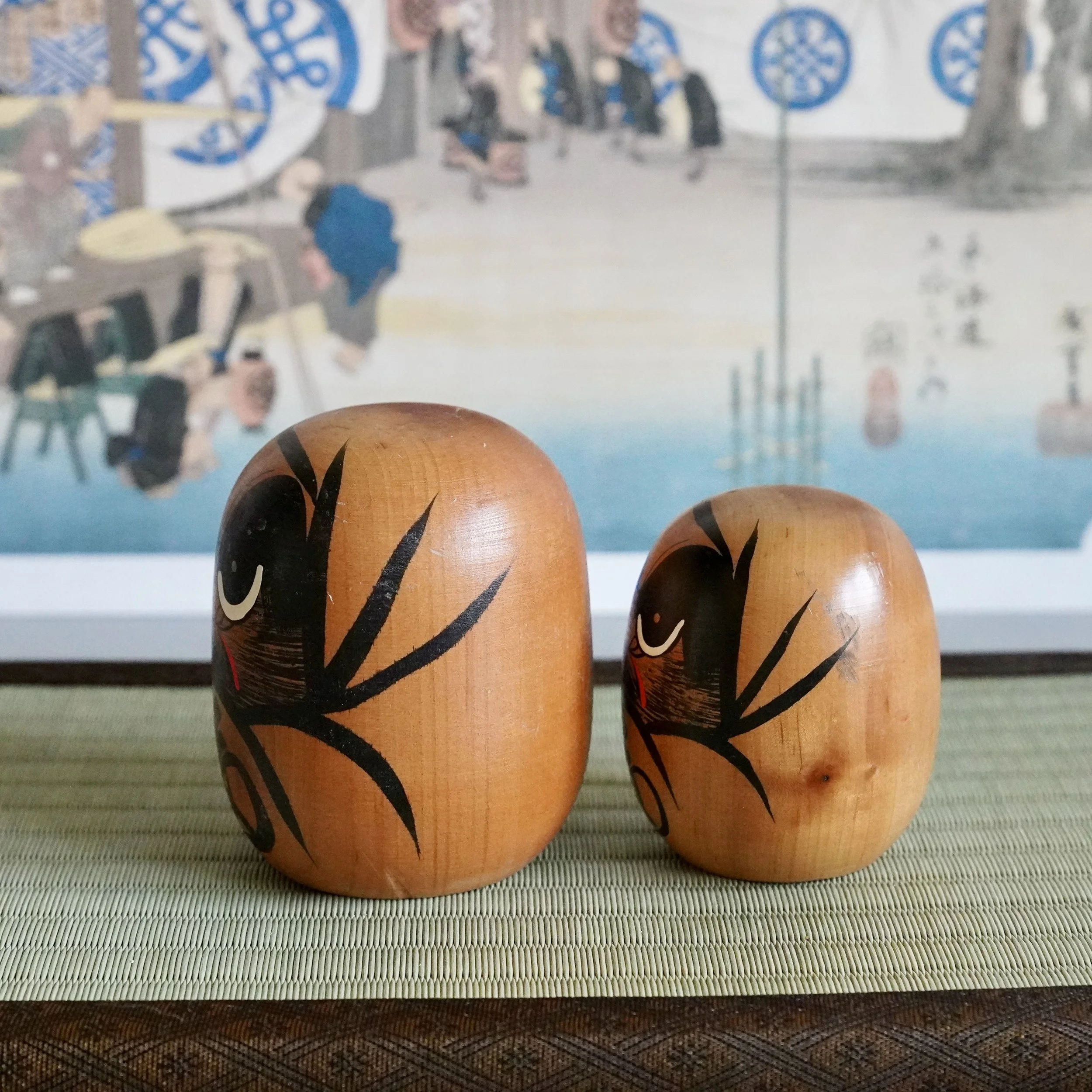 Angled view of a hand painted daruma pair, bamboo motif brushstroke along the body, vintage Japanese craft.