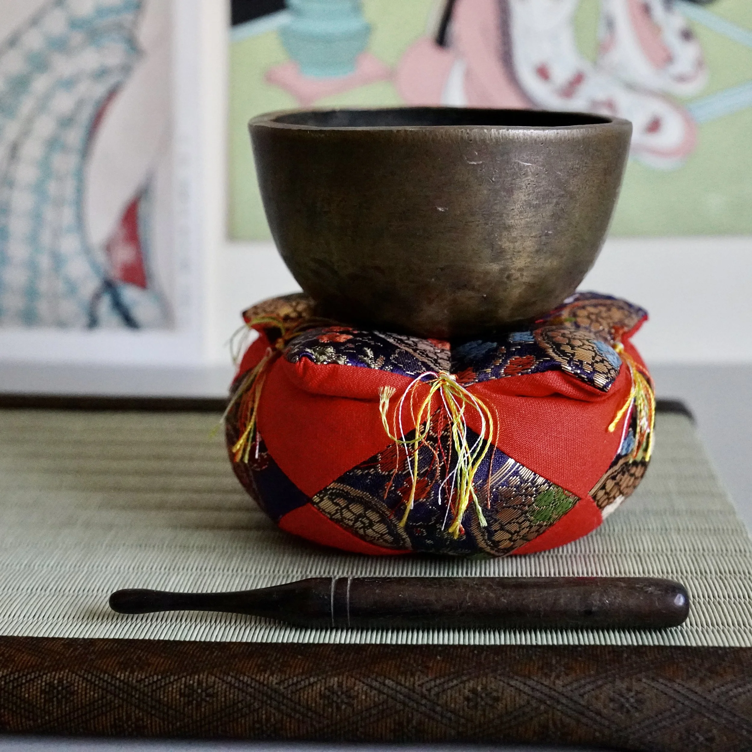 Small hand-hammered bronze orin singing bowl on brocade cushion with striker, tatami mat
