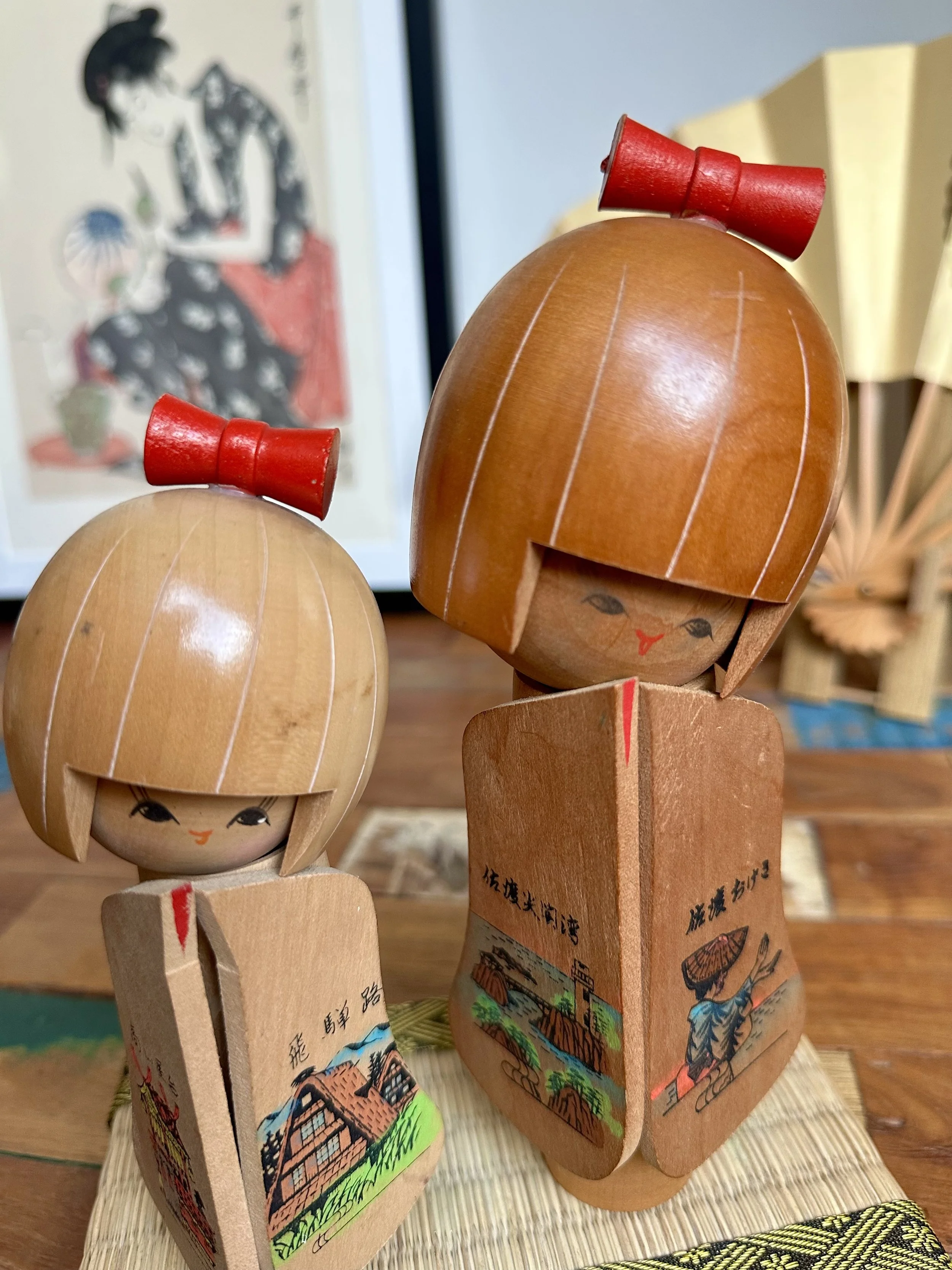 Overhead view omiyage kokeshi pair contrasting wood tones red hair bows cylindrical bases Japan
