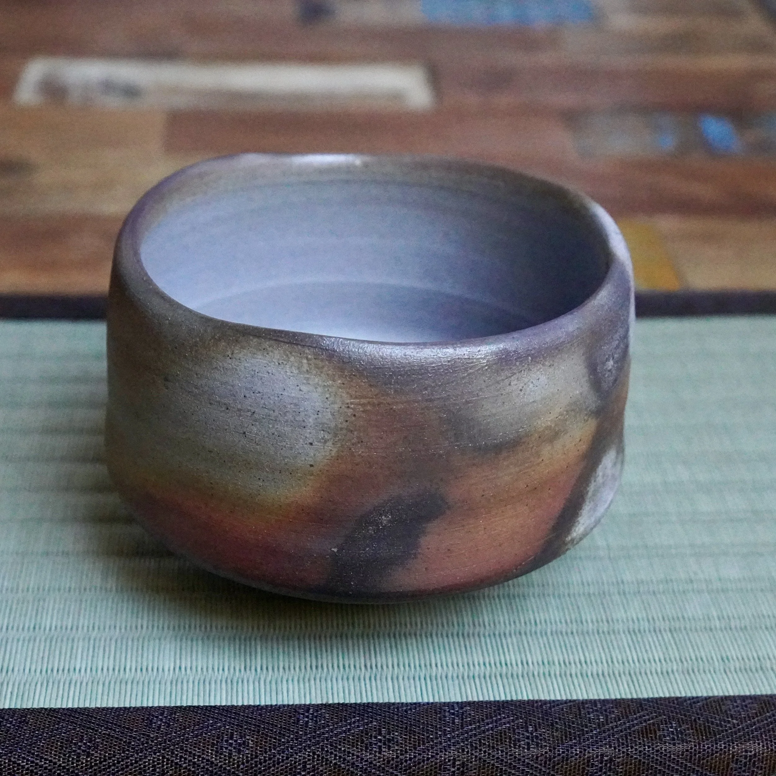 Inomata Masaaki's Sangiri Bizen chawan, featuring a rustic unglazed exterior with deep rust, burnt orange, and ash-grey tones, and a pale purplish-grey interior.