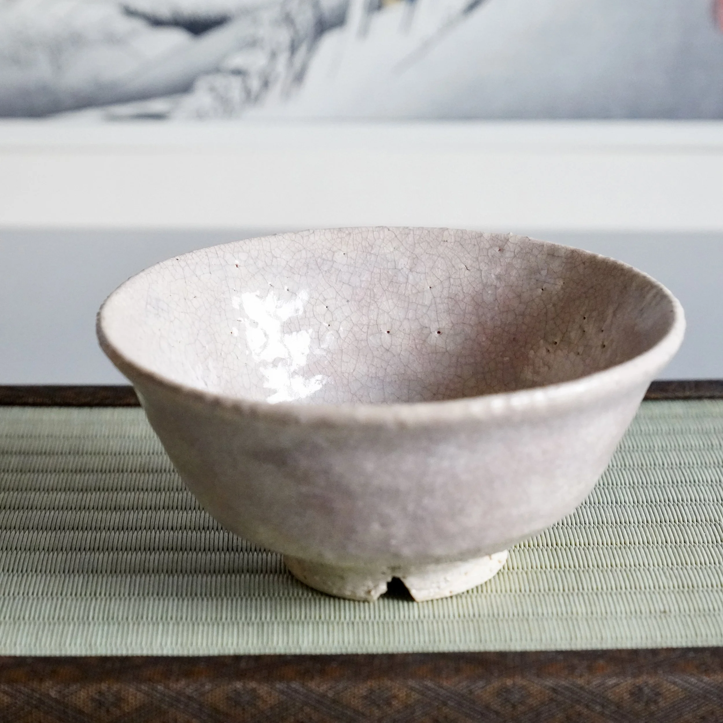 Hagi ware natsu-jawan matcha bowl on tatami mat, pale crackled glaze, ukiyoe print in background