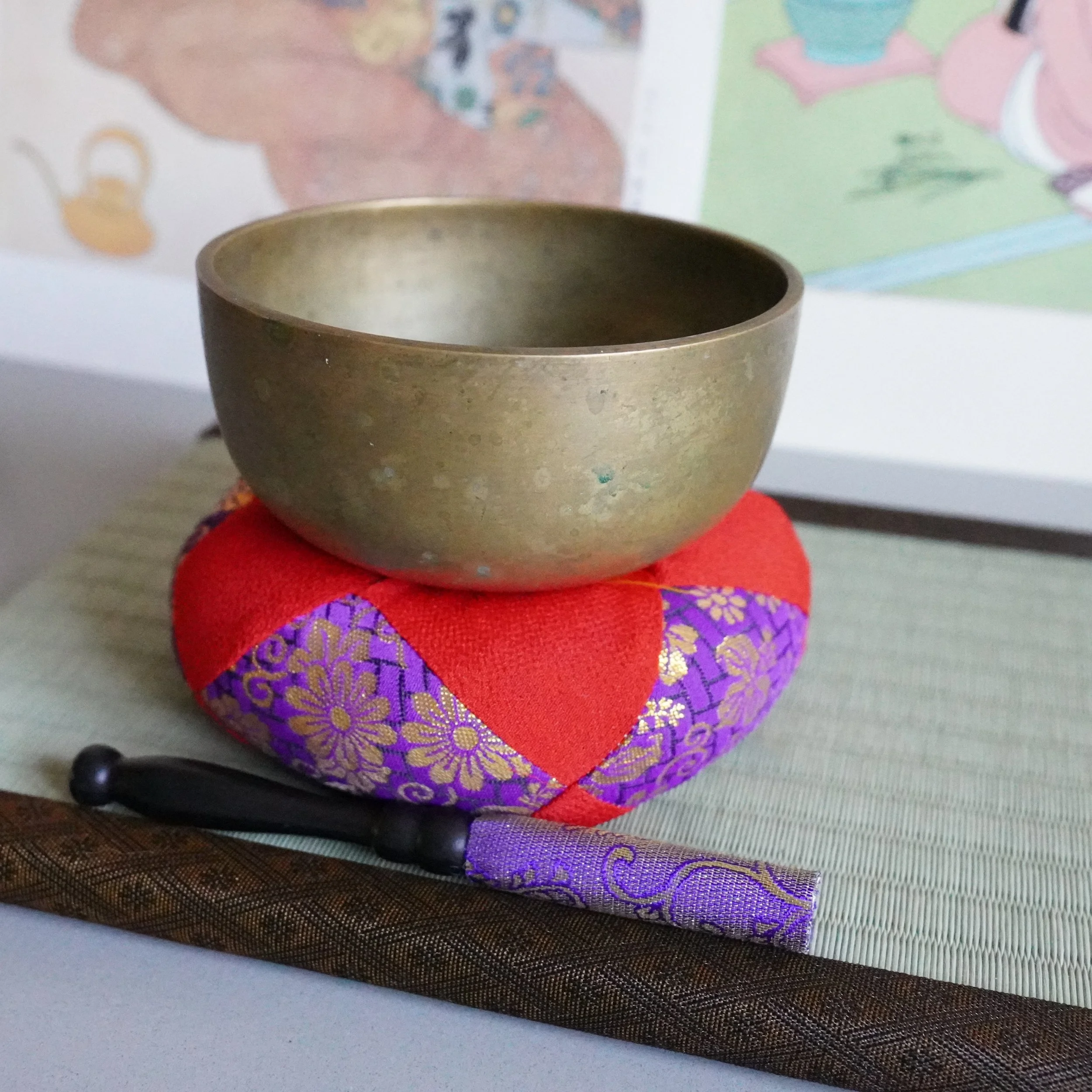 Side profile of bronze orin bowl on brocade cushion with striker, tatami mat