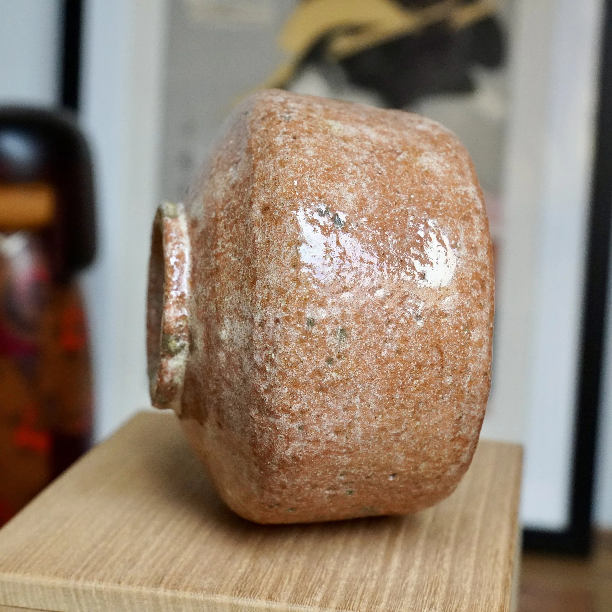 Red raku chawan resting on its side, featuring a rugged, pitted surface with white deposits and reflective glaze patches.