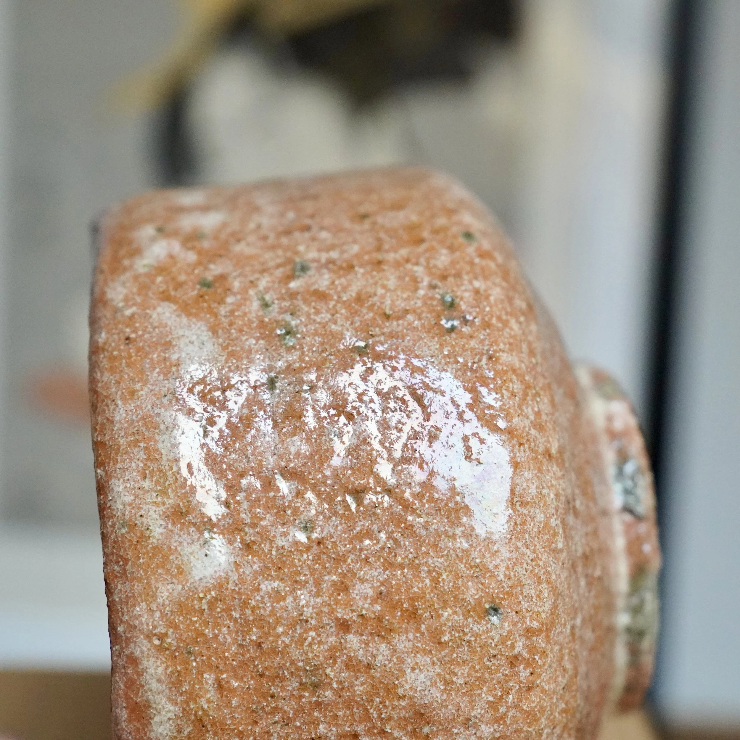 Detail of Sawada Hiroyuki's aka-raku chawan, featuring a reddish-orange, sandy, and pitted surface with a pale white glaze run and glossy areas.