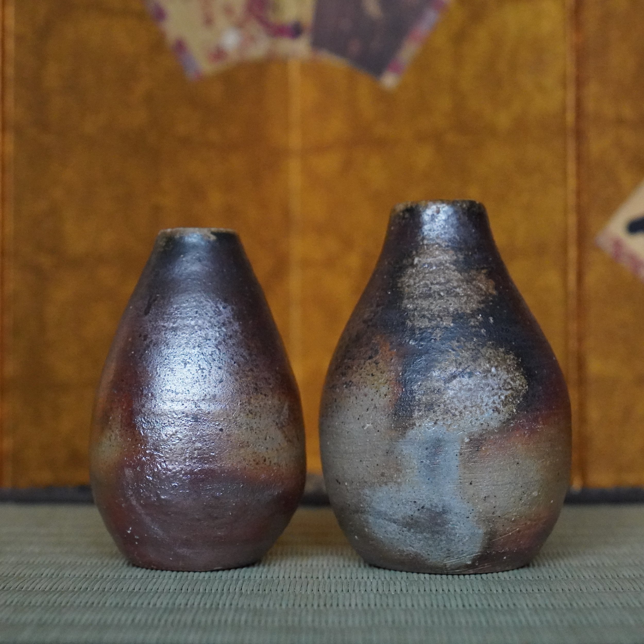 Front view of two Shibaoka Tōsendō Bizen-yaki tokkuri vases on a  tatami mat with silvery-blue and reddish-brown firing marks.