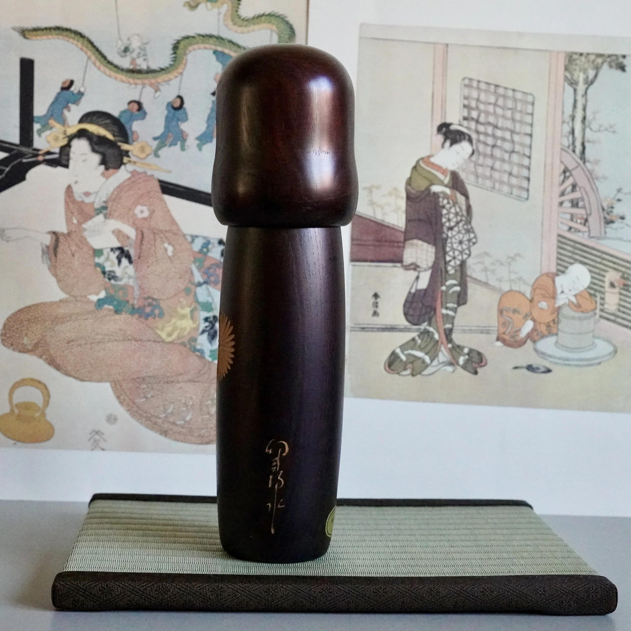 Usaburo kokeshi doll from angle showing gold carved signature on lower body, dark stained wood