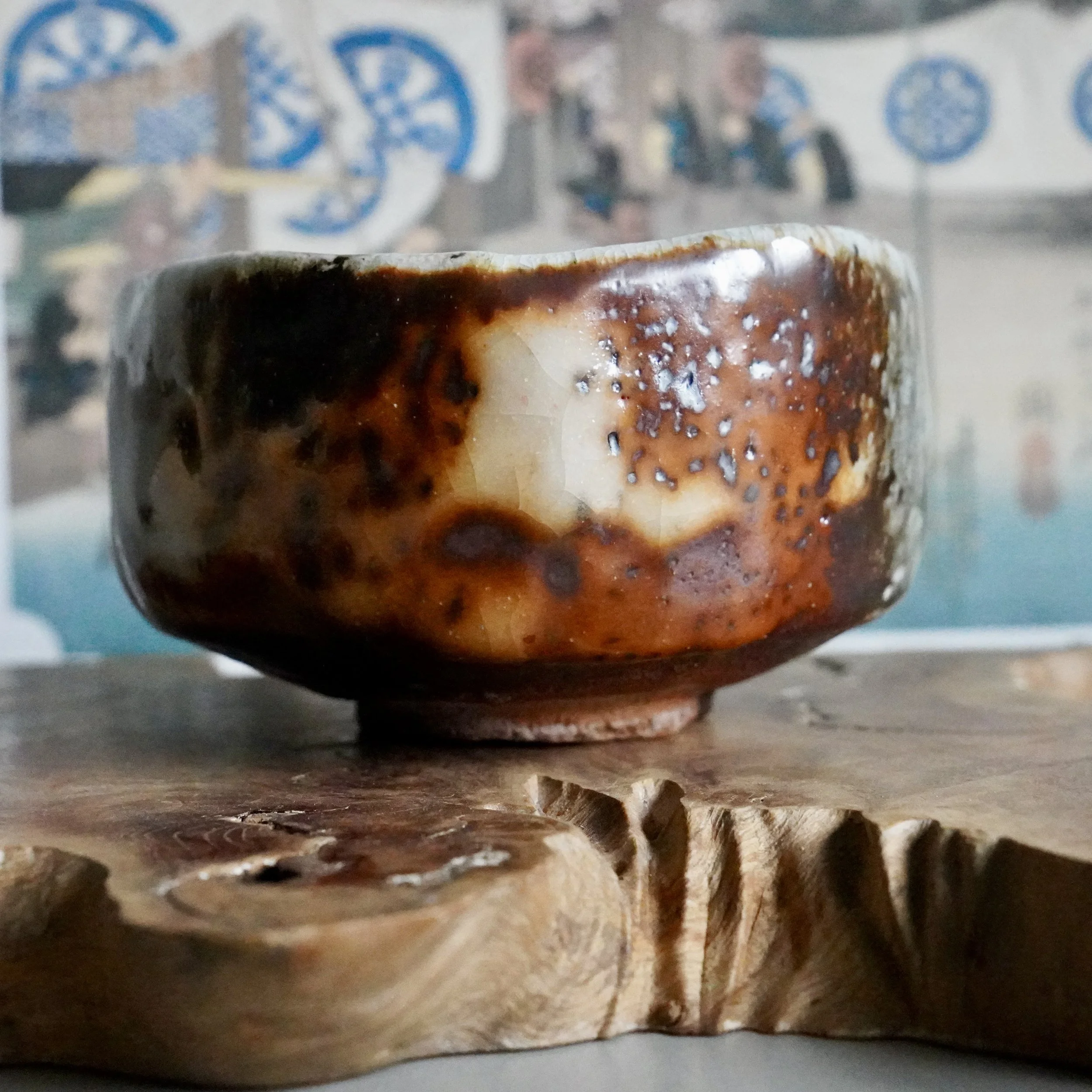 Deguchi Eiji wood-fired chawan with variegated rust-orange, dark brown, and finely crackled cream glaze, on a raw wood slab.