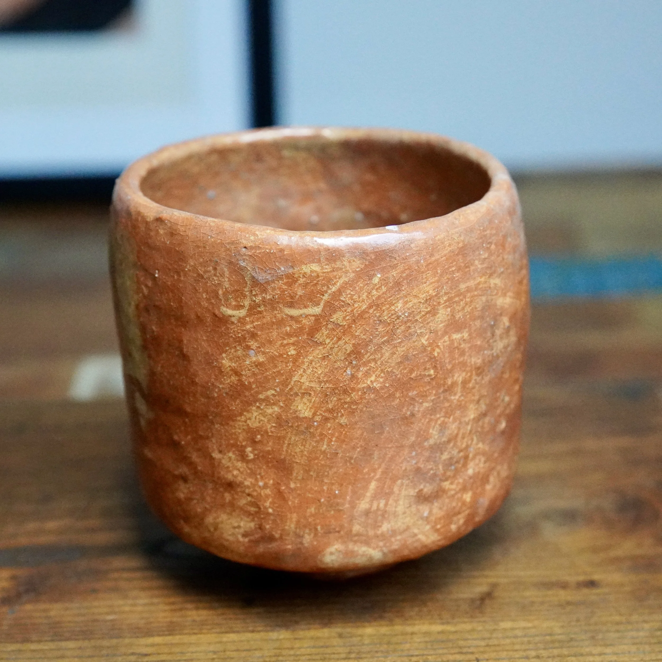 Tall, reddish-brown ceramic tsutsu chawan with fine crazing and irregular lighter patches. White drip glaze runs from the rim, fading halfway down one side.