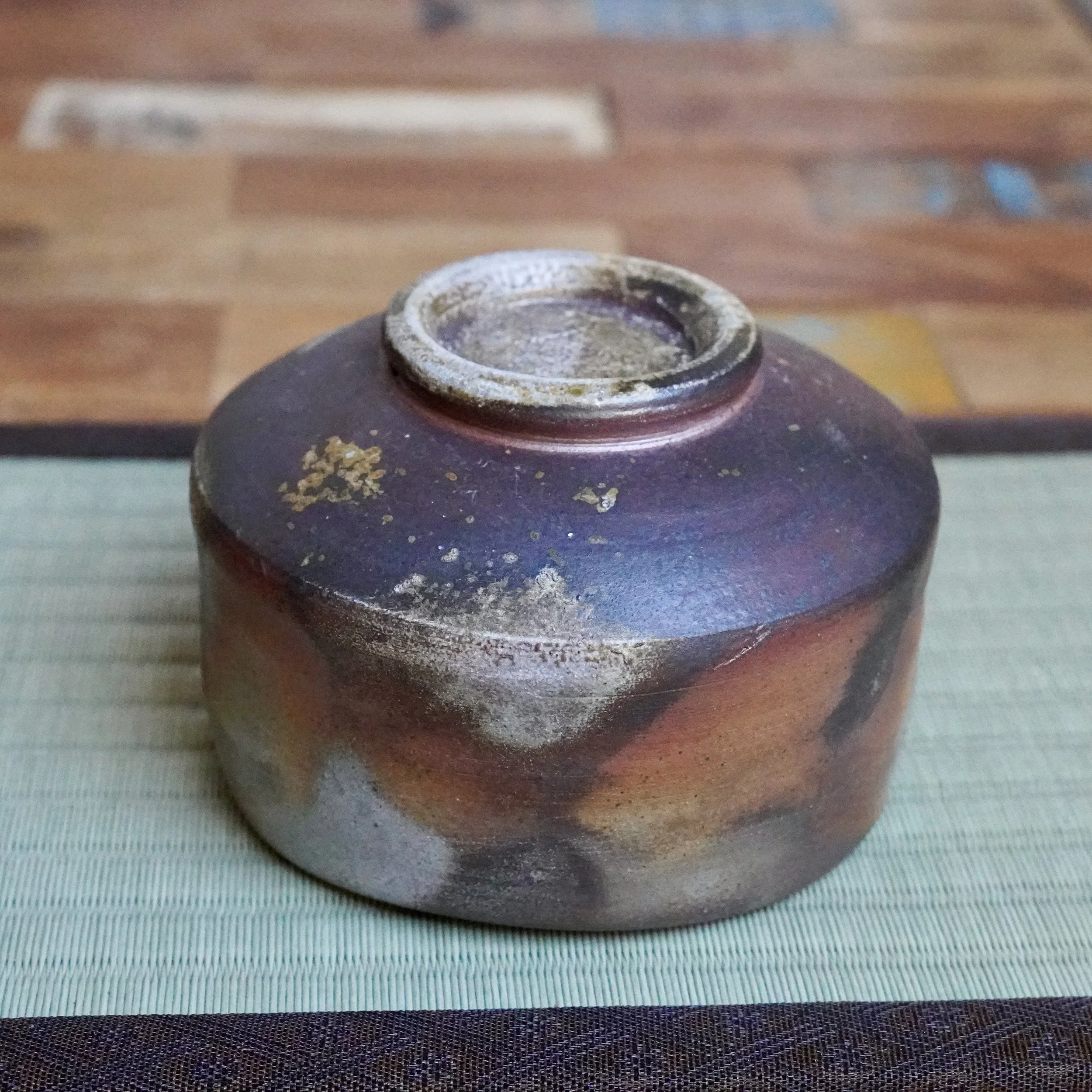 Inomata Masaaki's inverted Sangiri Bizen chawan, showing rust orange and ash grey fired clay with a silver-dusted rim, on a green mat.
