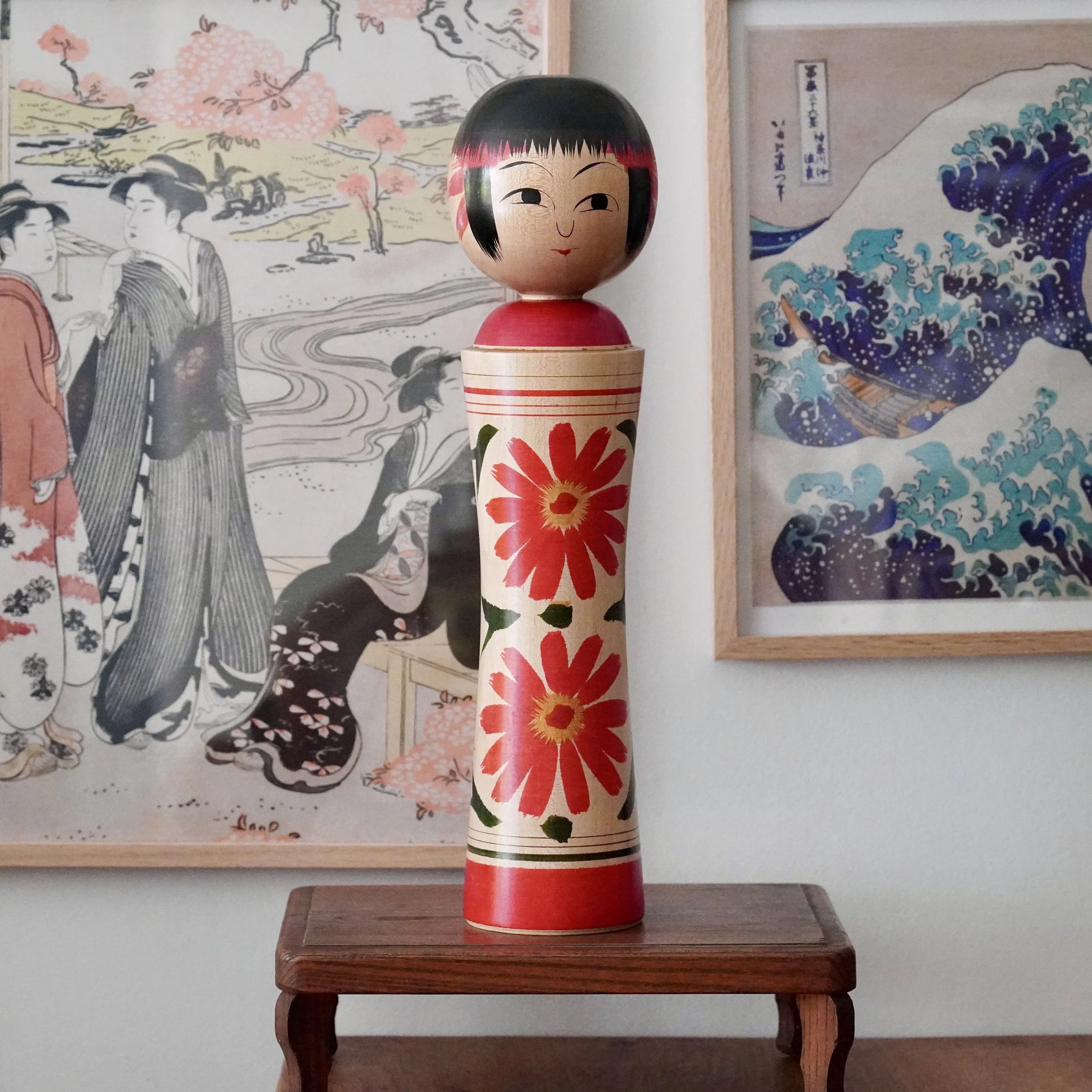 Tall Ginzan kokeshi by Izu Mamoru, front view. The wooden doll has a black bob, red face accents, and a painted face. Its pale body features two large red chrysanthemums, a red collar, and a red base.