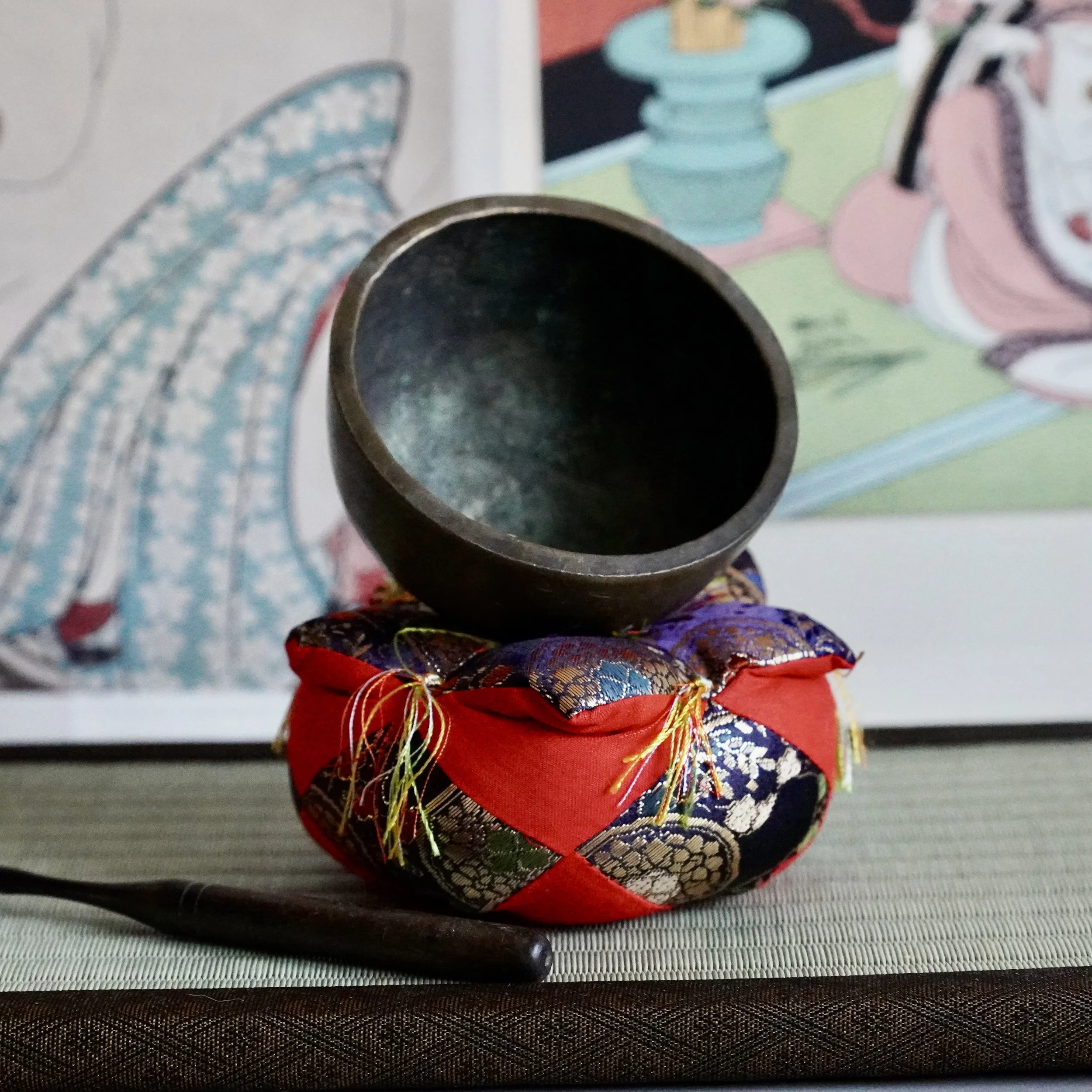 Small bronze orin singing bowl tilted to show hammered interior, brocade cushion