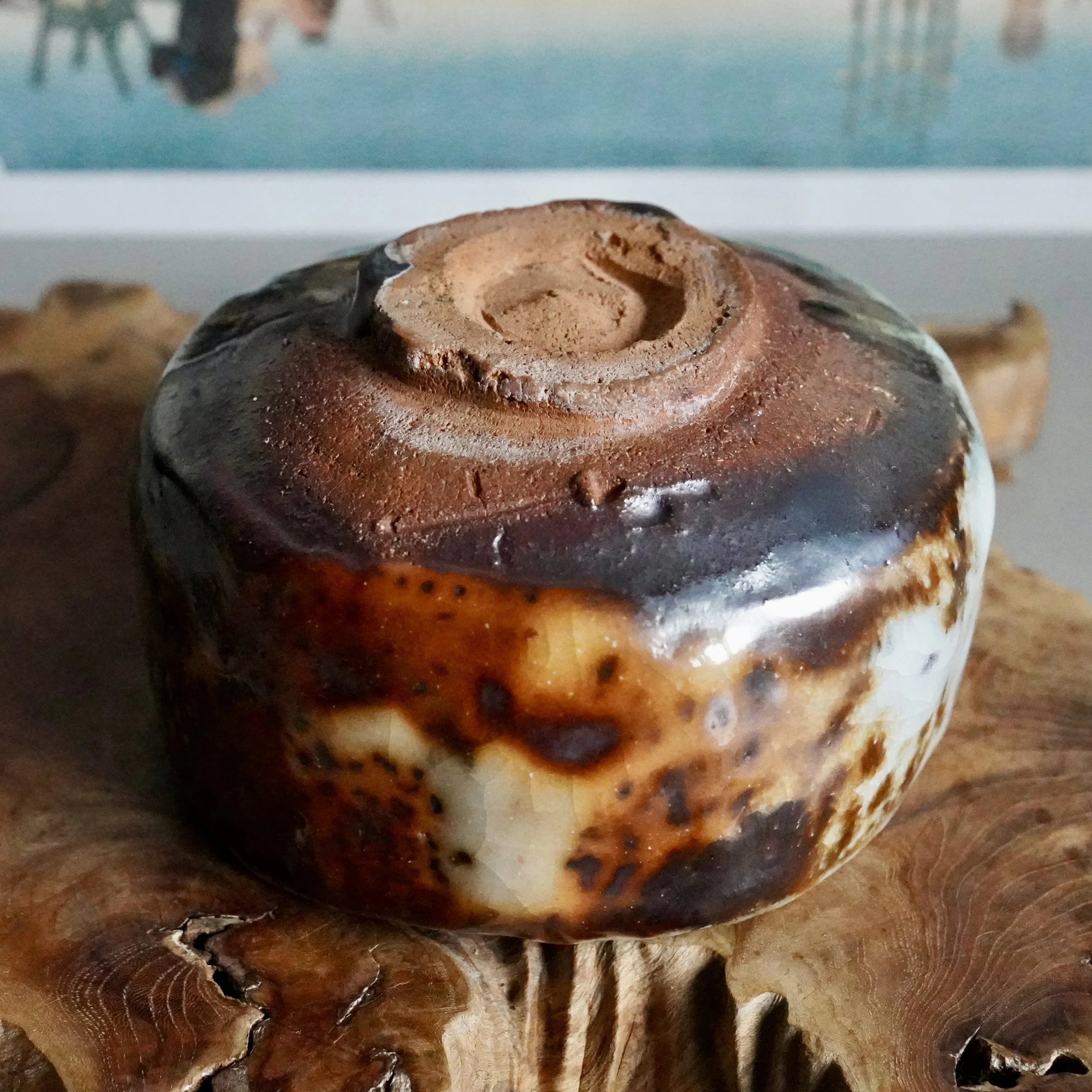 Deguchi Eiji wood-fired chawan base, unglazed reddish-brown foot and lower sides with mottled crackled white, orange, and dark glaze, on carved wood.