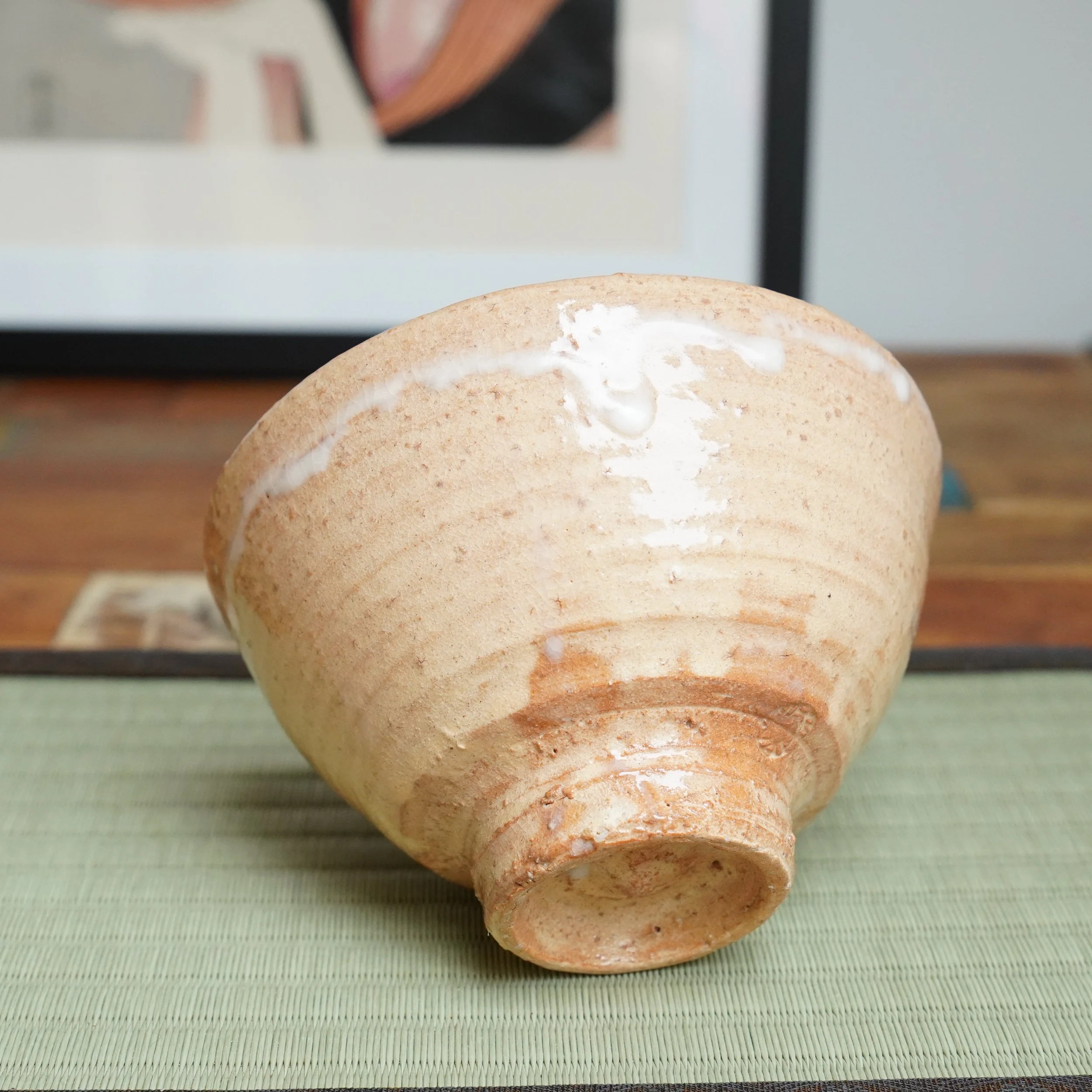 Hagi-yaki chawan by Kaneko Nobuhiko, side view, a salmon-pink body with a thick white glaze drip across the rim, showing crackled texture, on a green tatami mat.