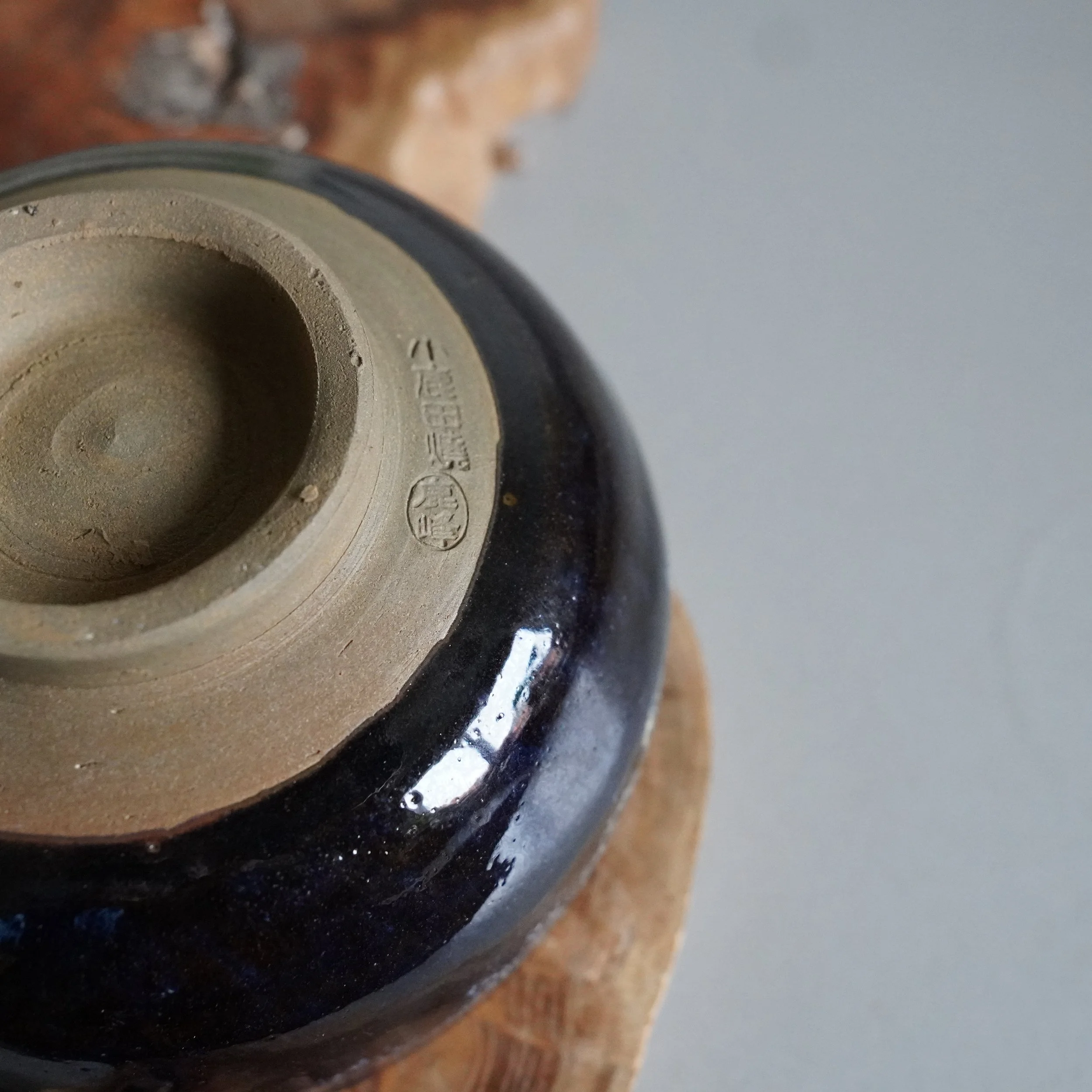 Underside of a glazed ceramic bowl, appearing dark brown and blue. The unglazed foot shows tan clay with a stamped potter's mark, 鹿峰 (Rokuhō).