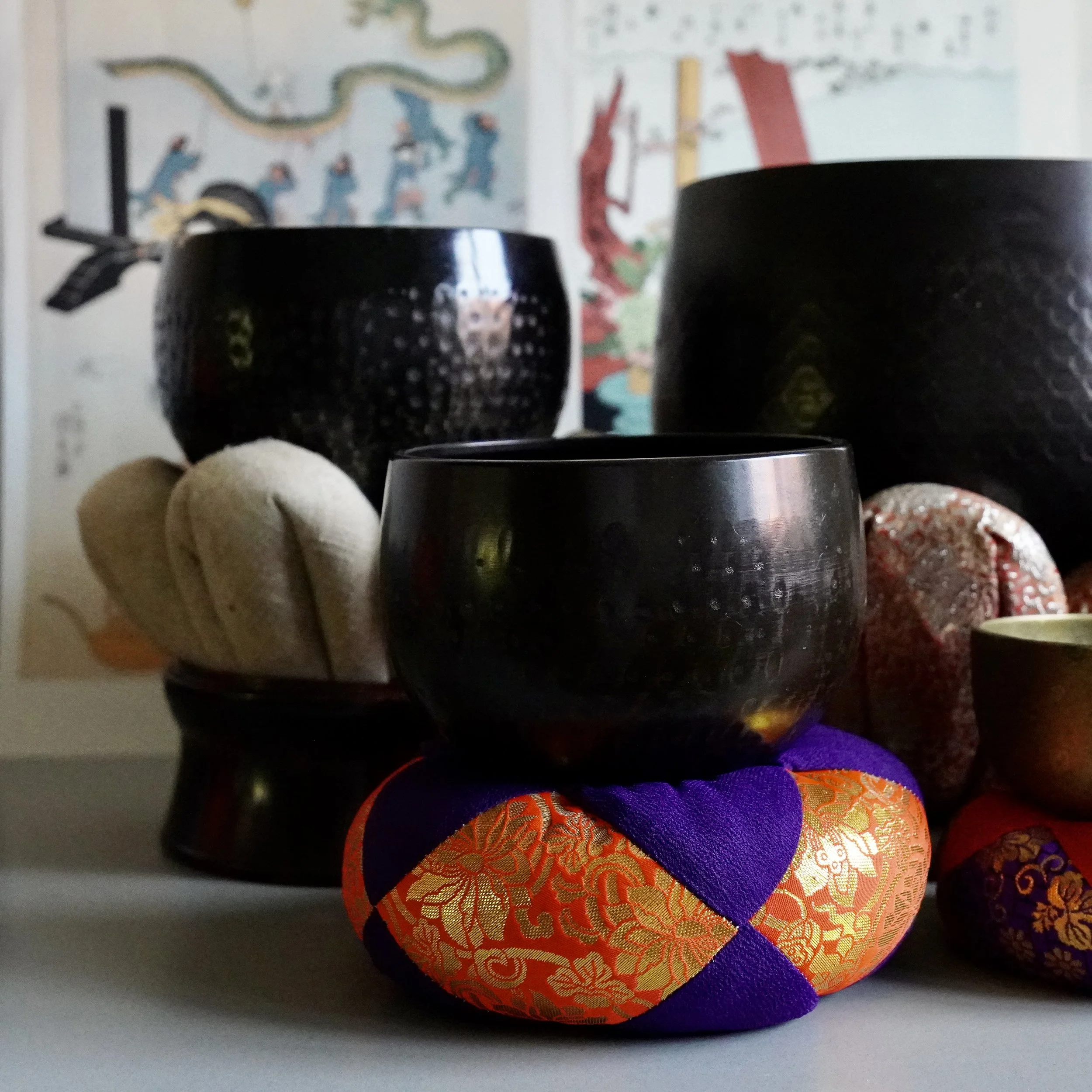 Group of vintage Japanese bronze orin singing bowls in different sizes, including the large hand-hammered temple-size bowl, displayed together on brocade cushions