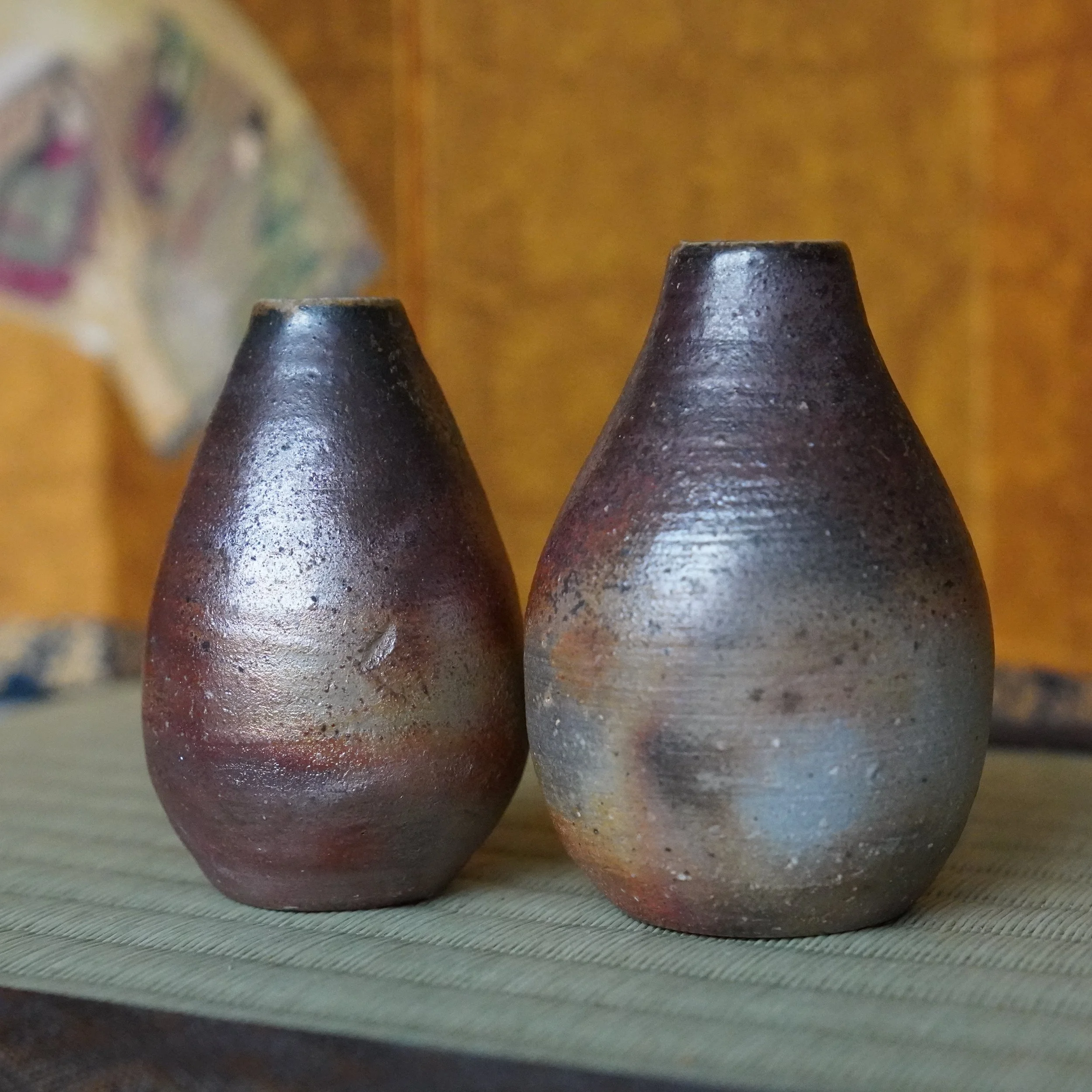Pair of textured Bizen-yaki tokkuri vases by Shibaoka Tōsendō, Kōzan-gama, displaying aubergine and silvery-grey tones on a woven mat.