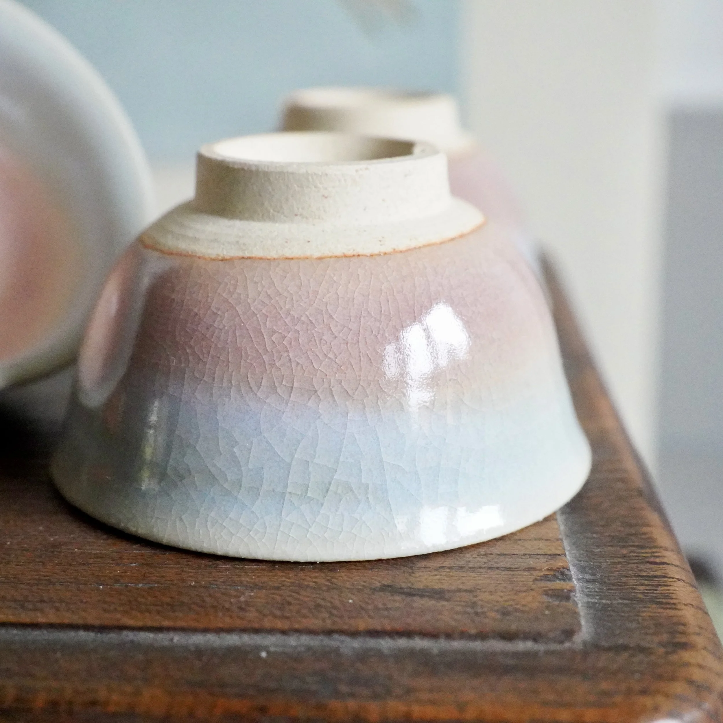 Upturned Hagi-yaki ochoko, blush to pale blue-grey gradient glaze with crazing, unglazed foot, on a dark wooden surface.